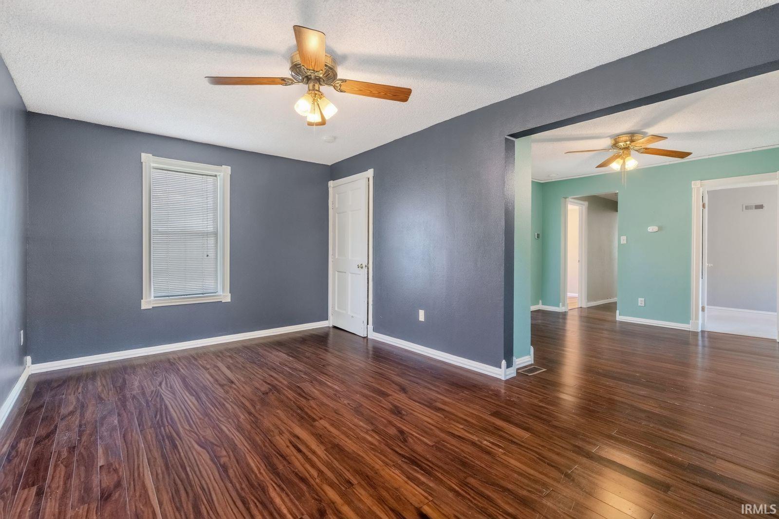 Interior room featuring rich wood-finish flooring, a ceiling fan with light fixture, and a window with blinds