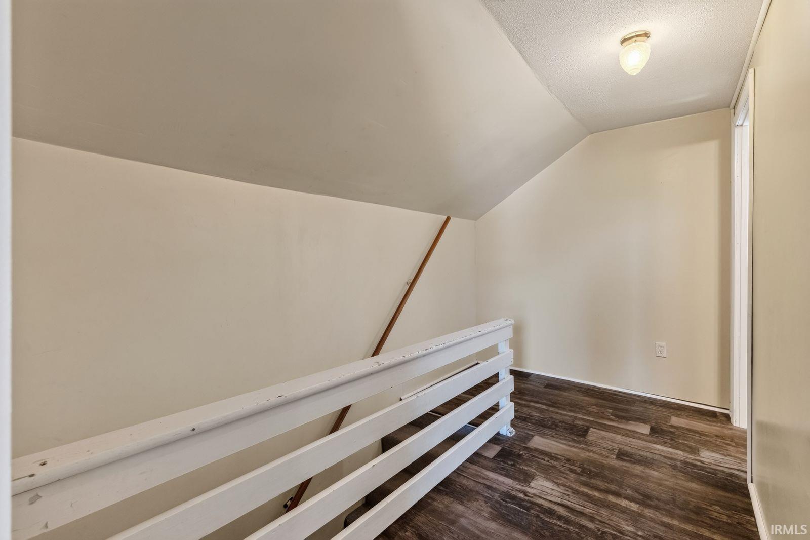 Attic space featuring wood-finish flooring, a white railing, and an overhead light fixture