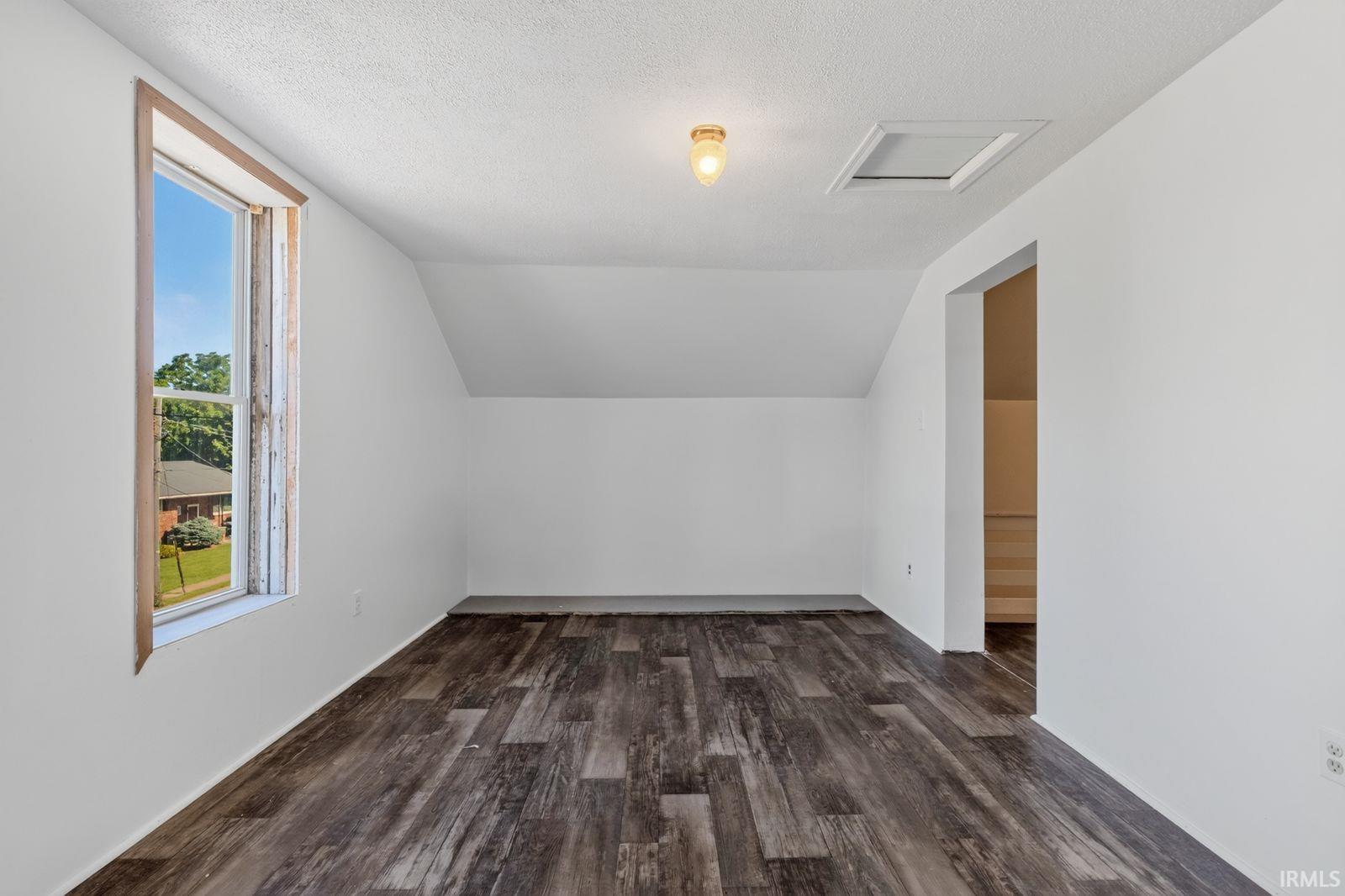 Spacious room featuring wood-finish flooring, white painted walls, and a sloped ceiling