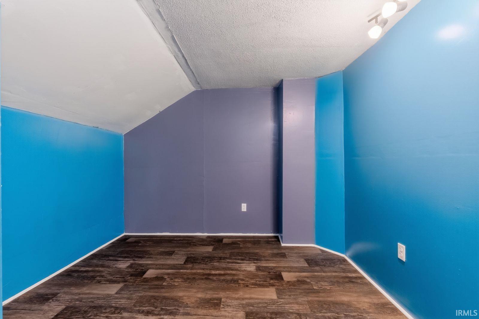 Room featuring wood-finish flooring, vibrant blue and muted purple walls, a textured white ceiling, and track lighting