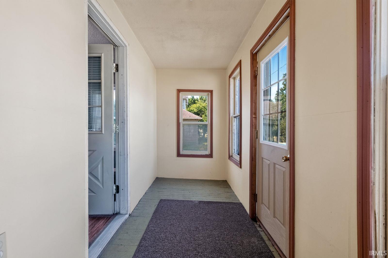 Enclosed front porch featuring two exterior doors, multiple pane windows with wood trim, and a dark floor covering
