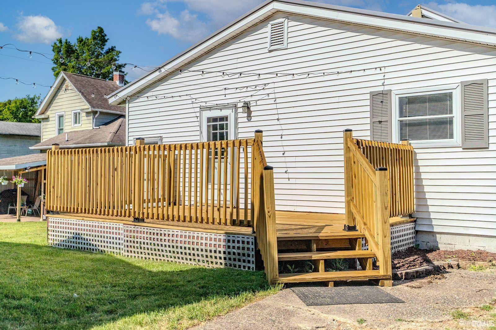 Rear white siding exterior featuring a natural wood deck with railings and steps