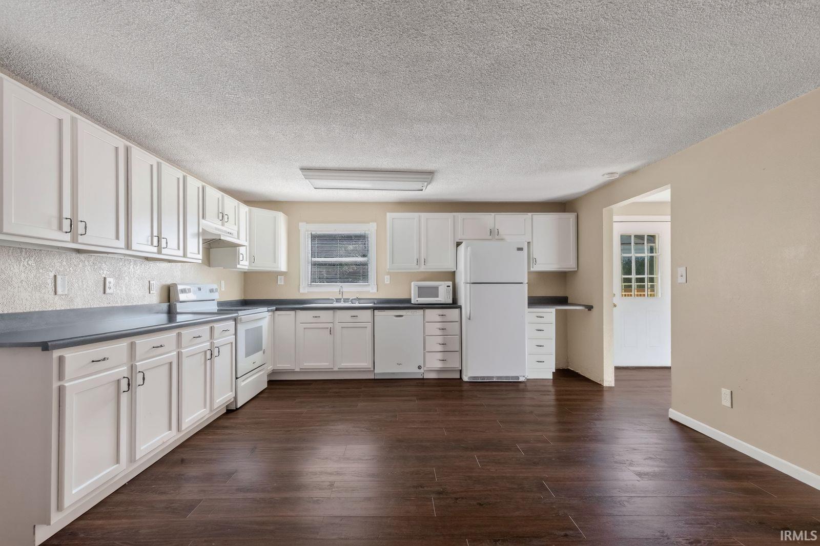Spacious kitchen featuring extensive white cabinetry, dark countertops, white built-in appliances, and wood-finish flooring