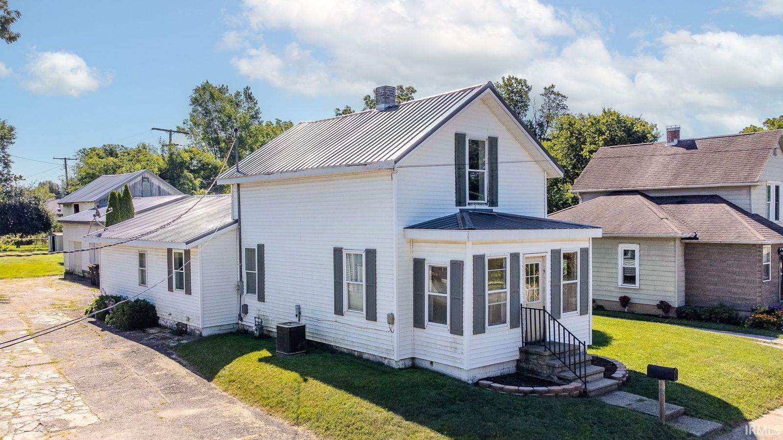 White siding residence featuring a corrugated metal roof, a covered front porch with iron railings, and a side-entry concrete driveway