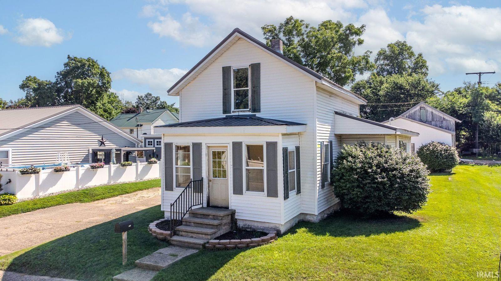 Traditional white siding exterior with dark shutters, a covered porch entrance, and a sloped roofline