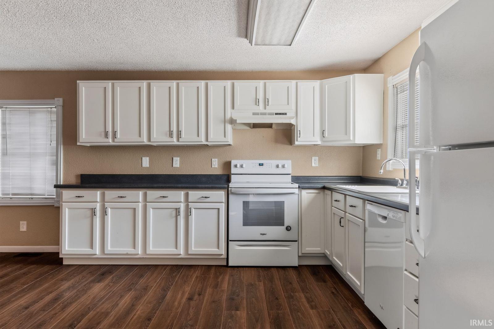 Kitchen featuring white cabinetry, dark countertops, wood-finish flooring, a white electric range, and a white dishwasher