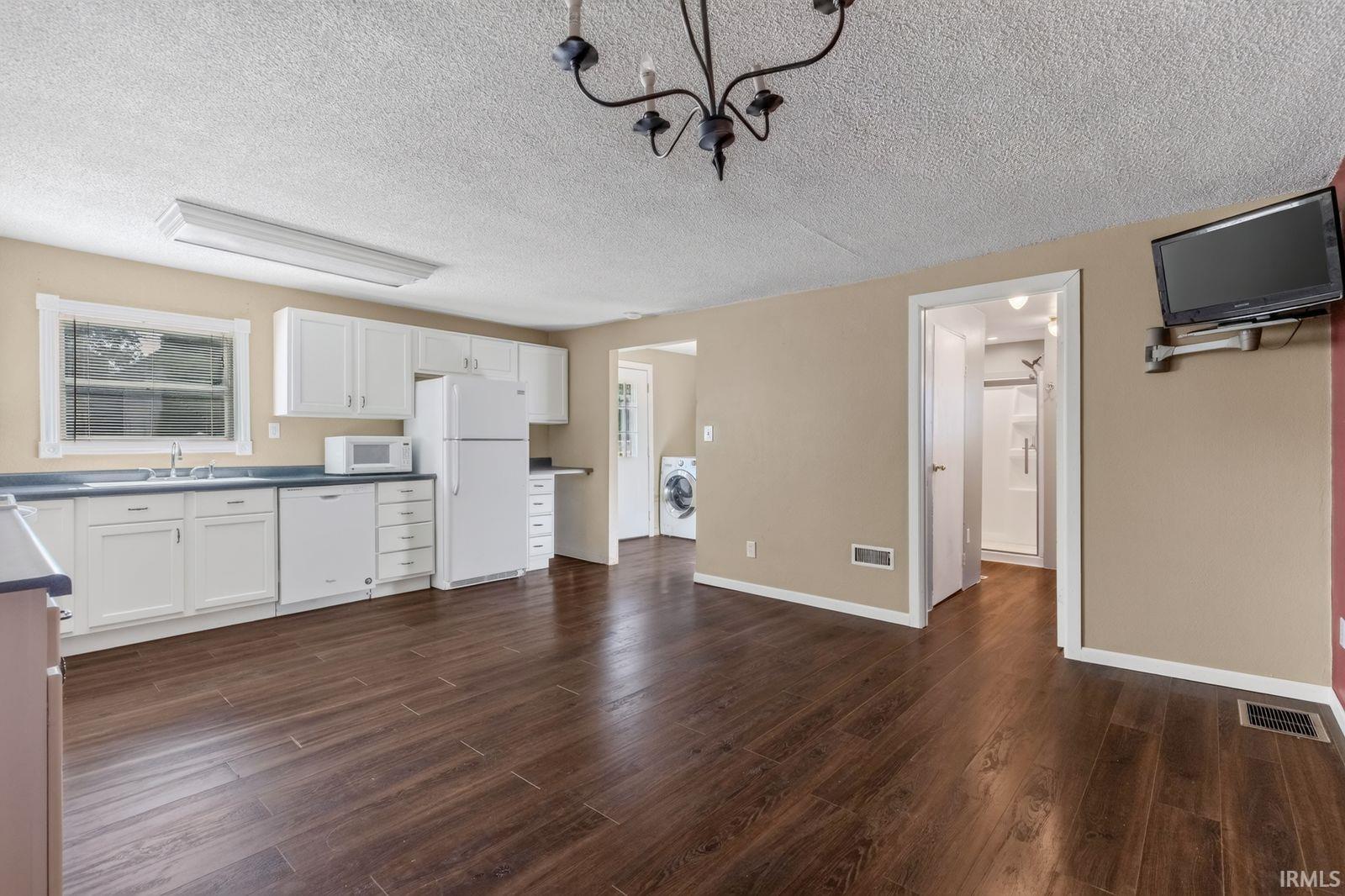 Open-concept kitchen and living area featuring wood-finish flooring, white cabinetry, and contrasting dark countertops