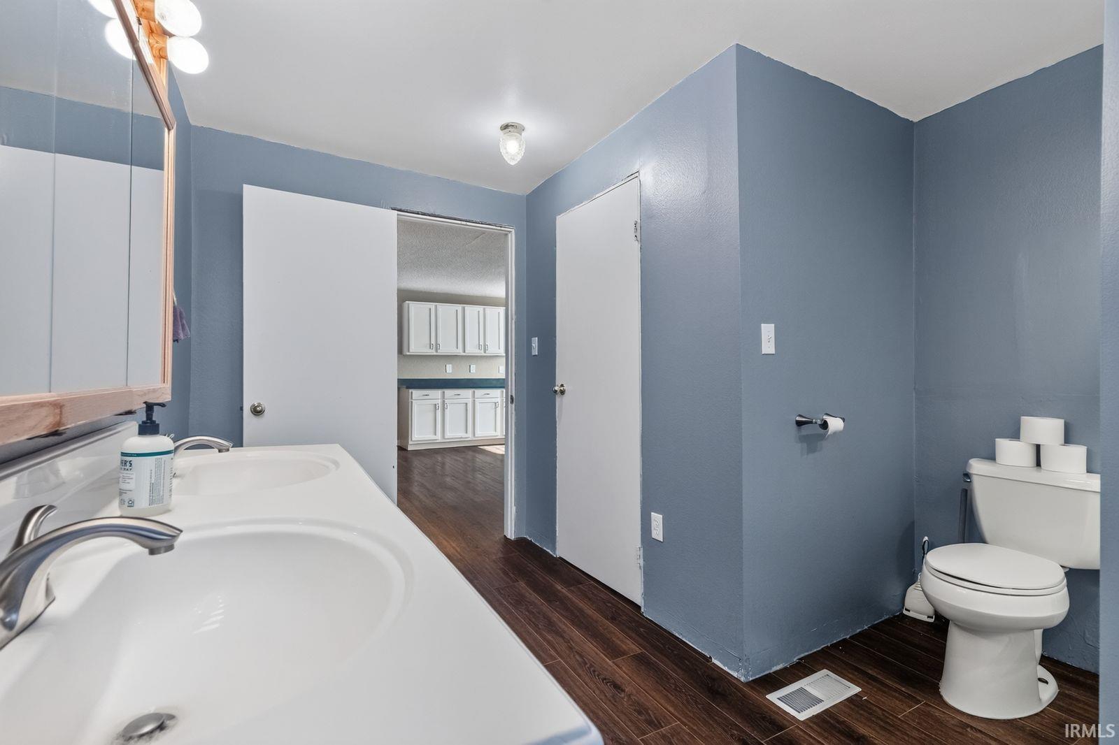 Bathroom featuring a dual vanity with white sinks and brushed nickel faucets, wood-finish flooring, and a white toilet