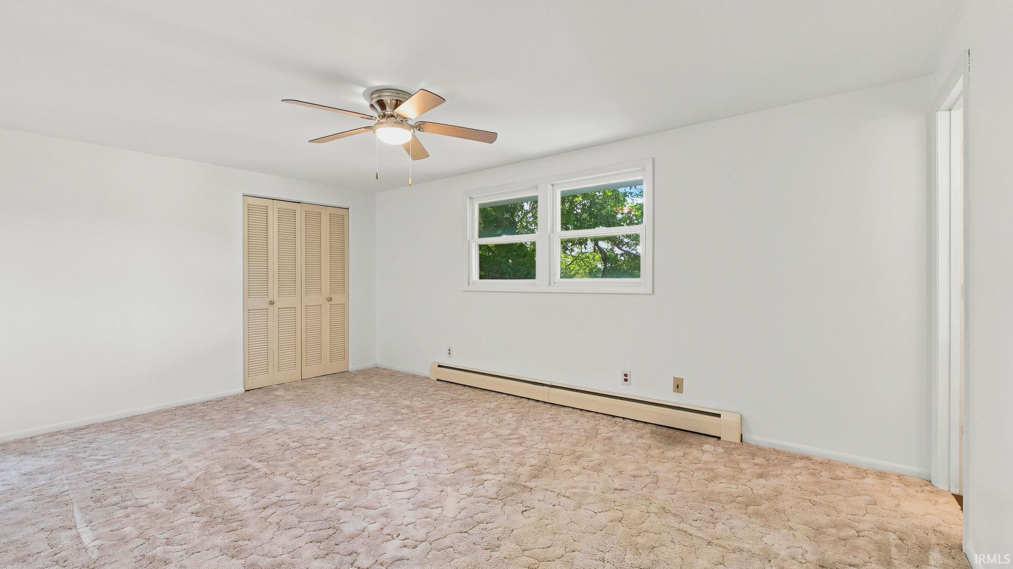 Carpeted room featuring a ceiling fan with integrated lighting, a window with exterior views, baseboard heating, and louvered bi-fold closet doors
