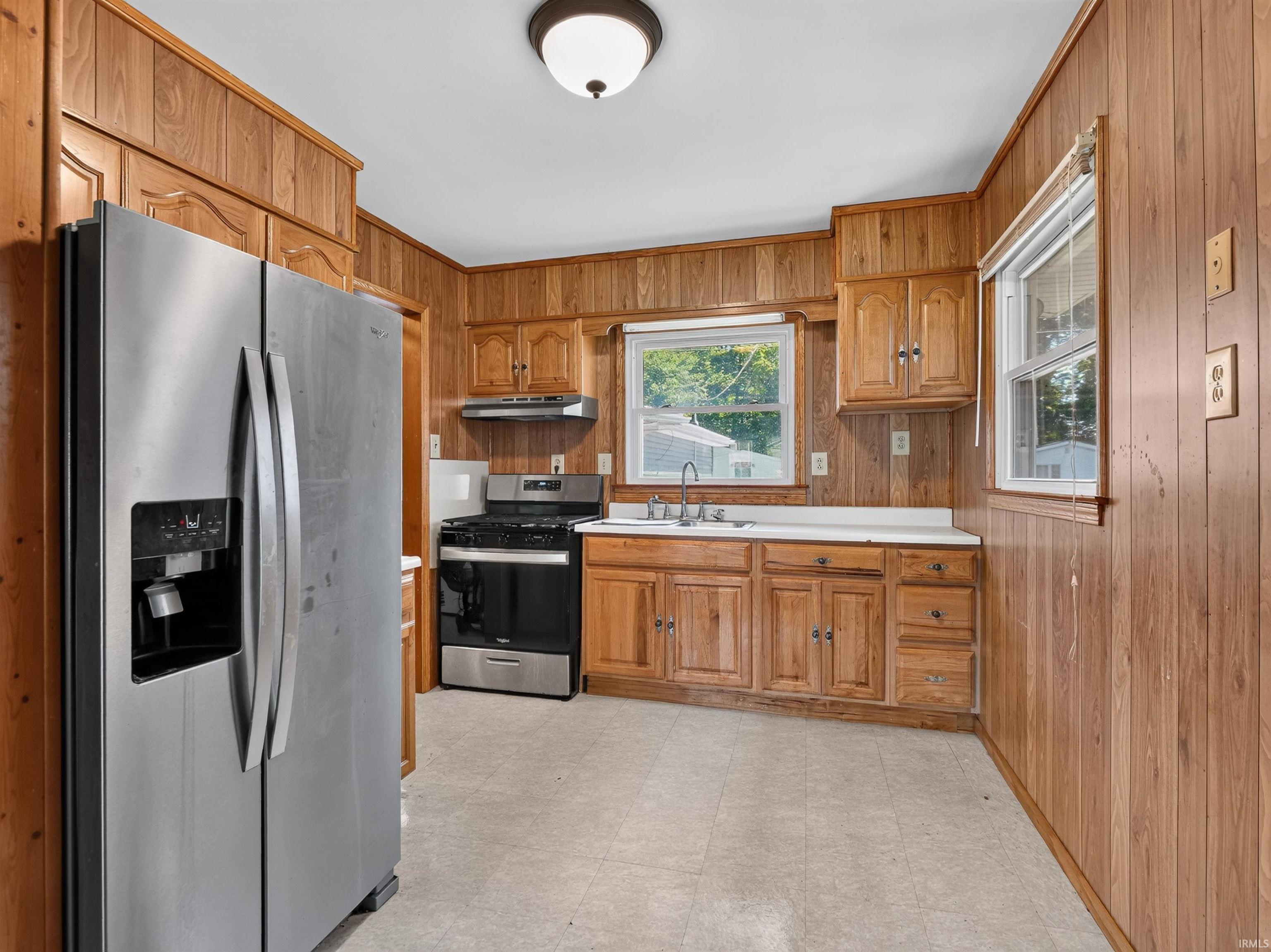 Kitchen featuring wood-paneled walls and cabinetry, white countertops, and a double basin sink