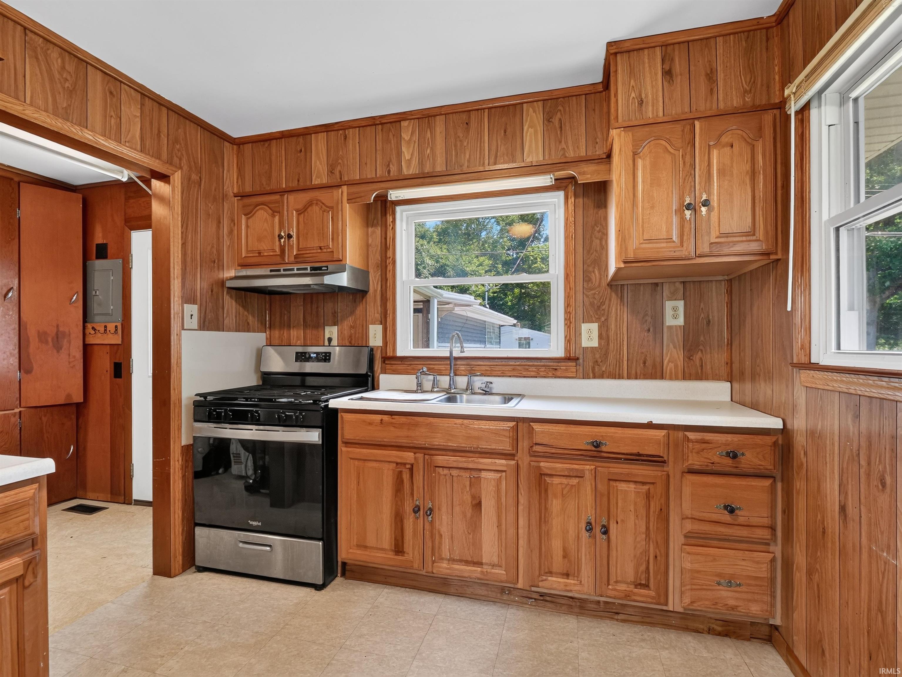 Kitchen featuring wood paneling, wood cabinetry, a stainless steel range with overhead hood, a stainless steel sink, and white countertops
