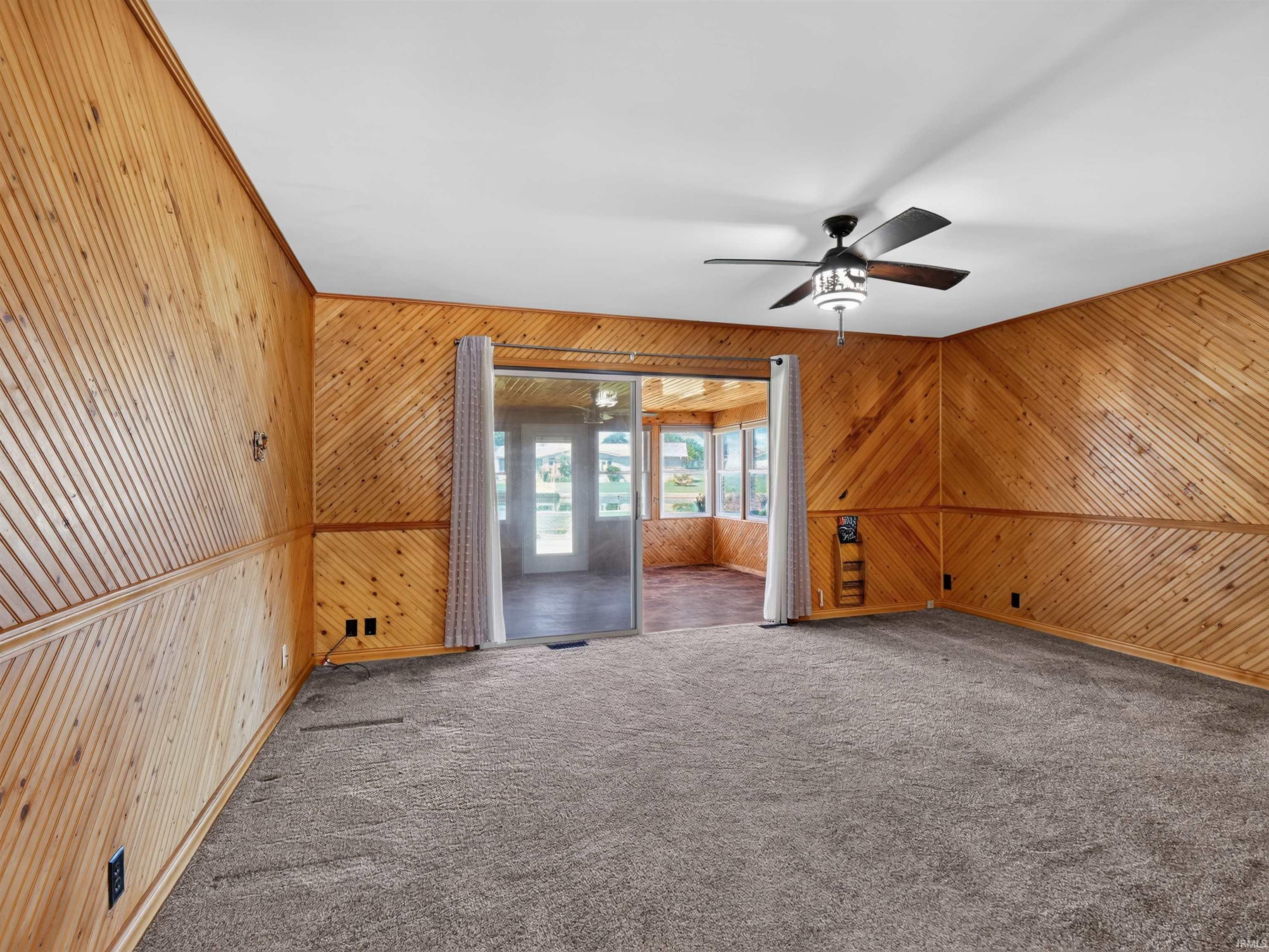 Carpeted interior space featuring wood-paneled walls with decorative trim and a ceiling fan with integrated lighting