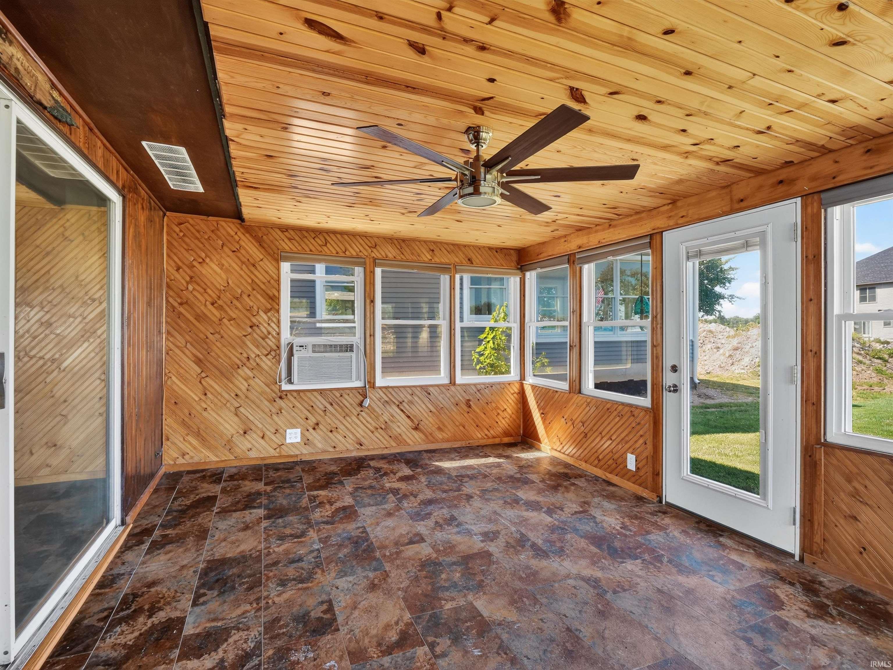 Sunroom featuring natural wood paneling throughout, multiple windows, a ceiling fan, and tile-finish flooring