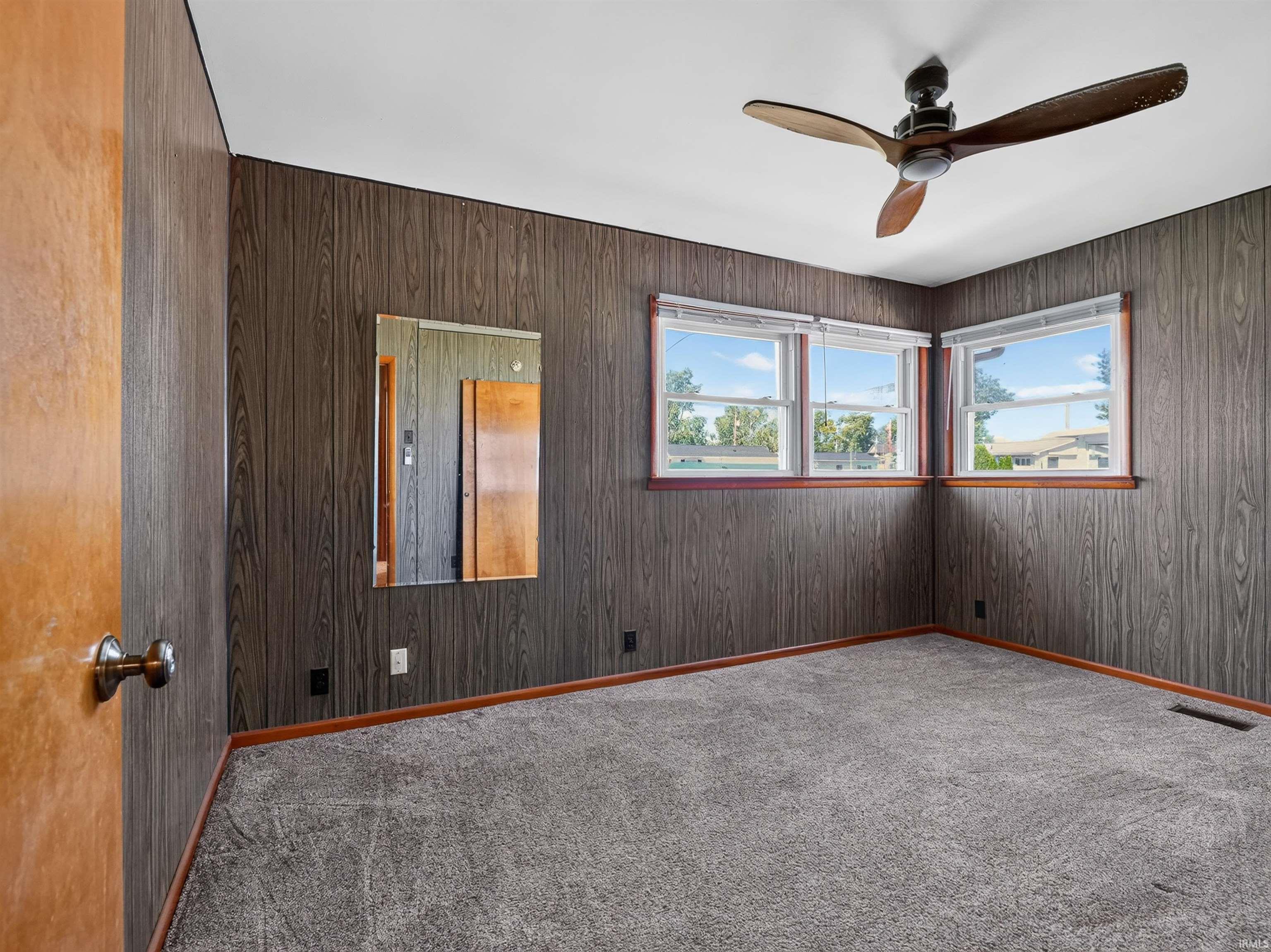 Corner room with dark wood-panel walls and light grey carpeting