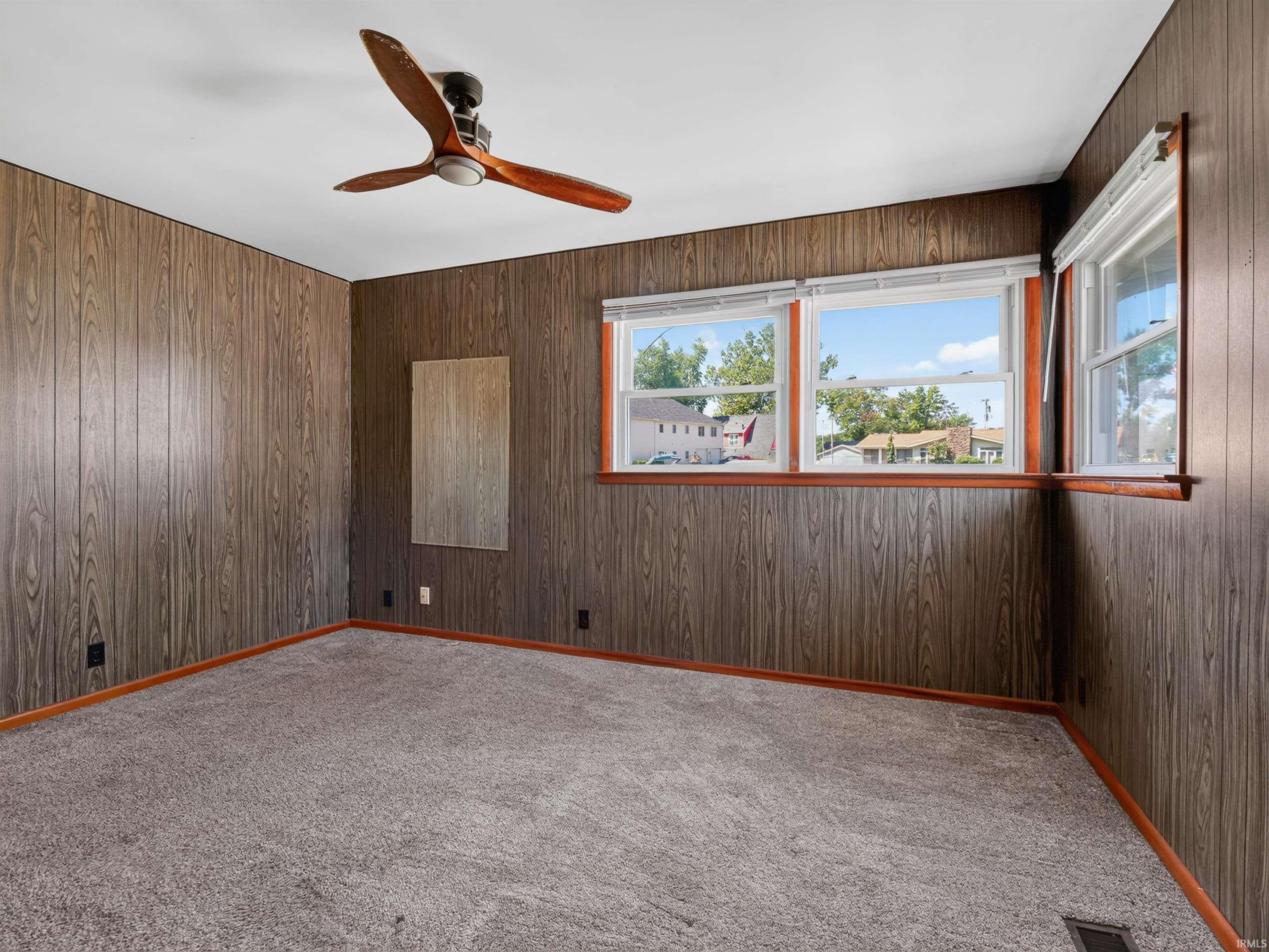 Carpeted room featuring wood-look paneling, a ceiling fan with wood-finish blades, and multiple windows with wood trim