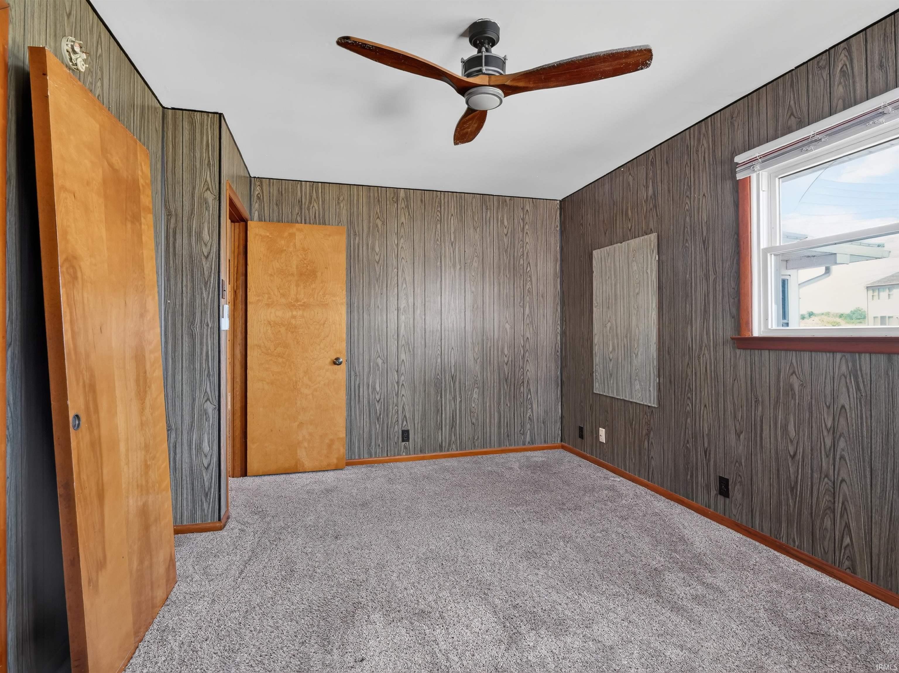 Bedroom featuring wood-finish paneling, light gray carpeting, and a ceiling fan