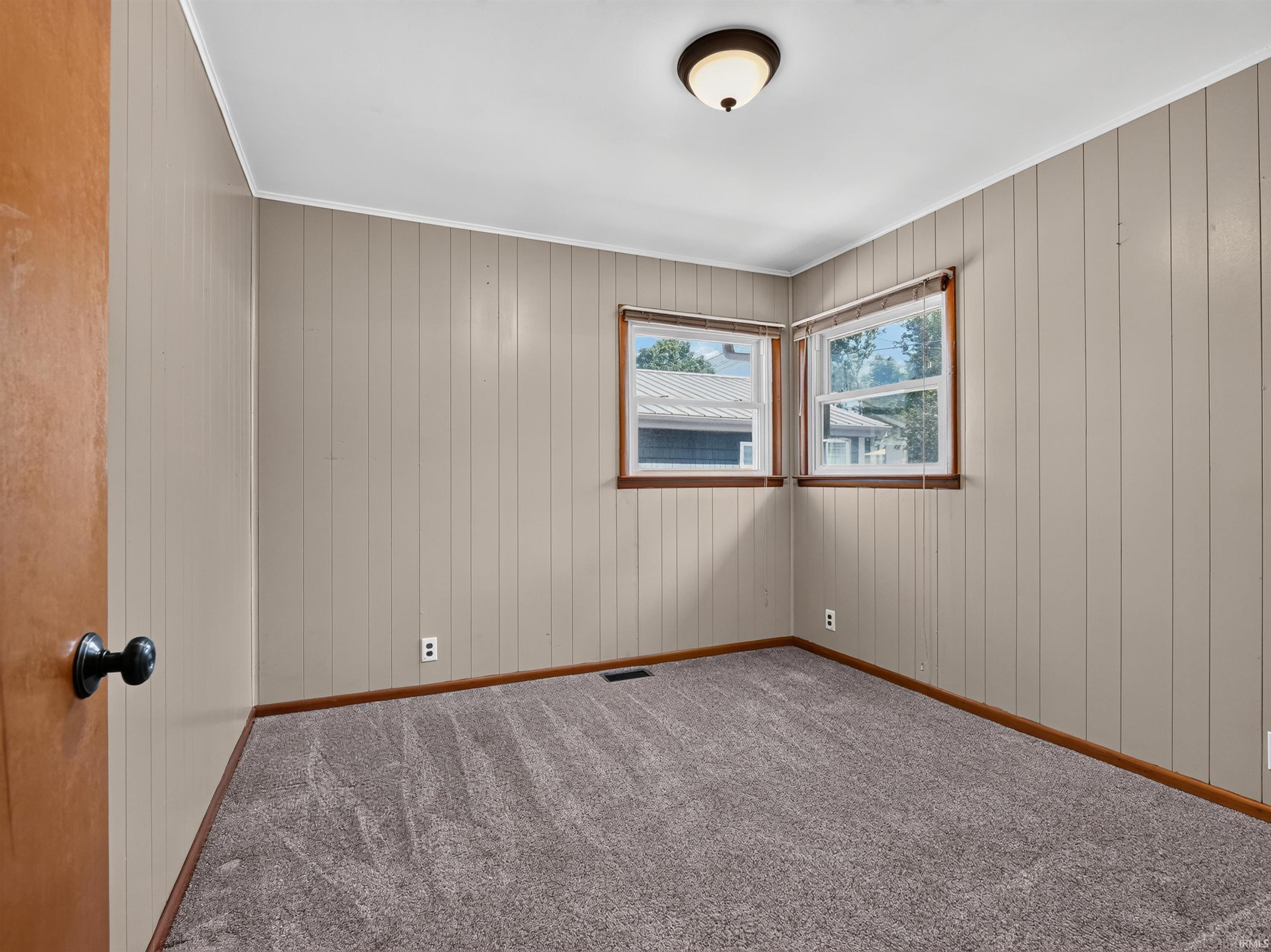 Neutral tone wall paneling, two windows with wood trim, and a flush mount ceiling light fixture