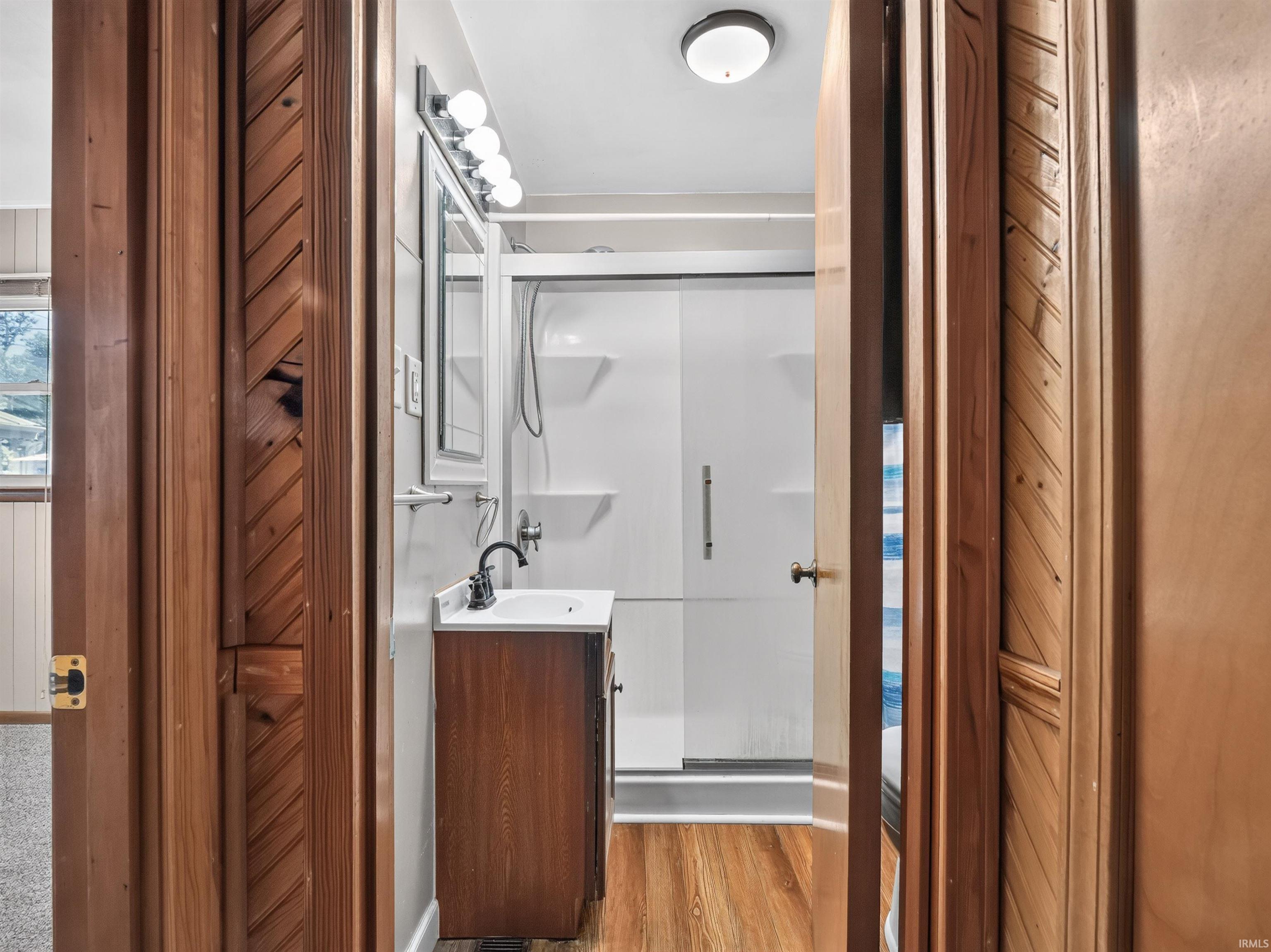 Bathroom featuring a dark wood-finish vanity with a white sink, matte black faucet, and a wall-mounted mirror with overhead lighting