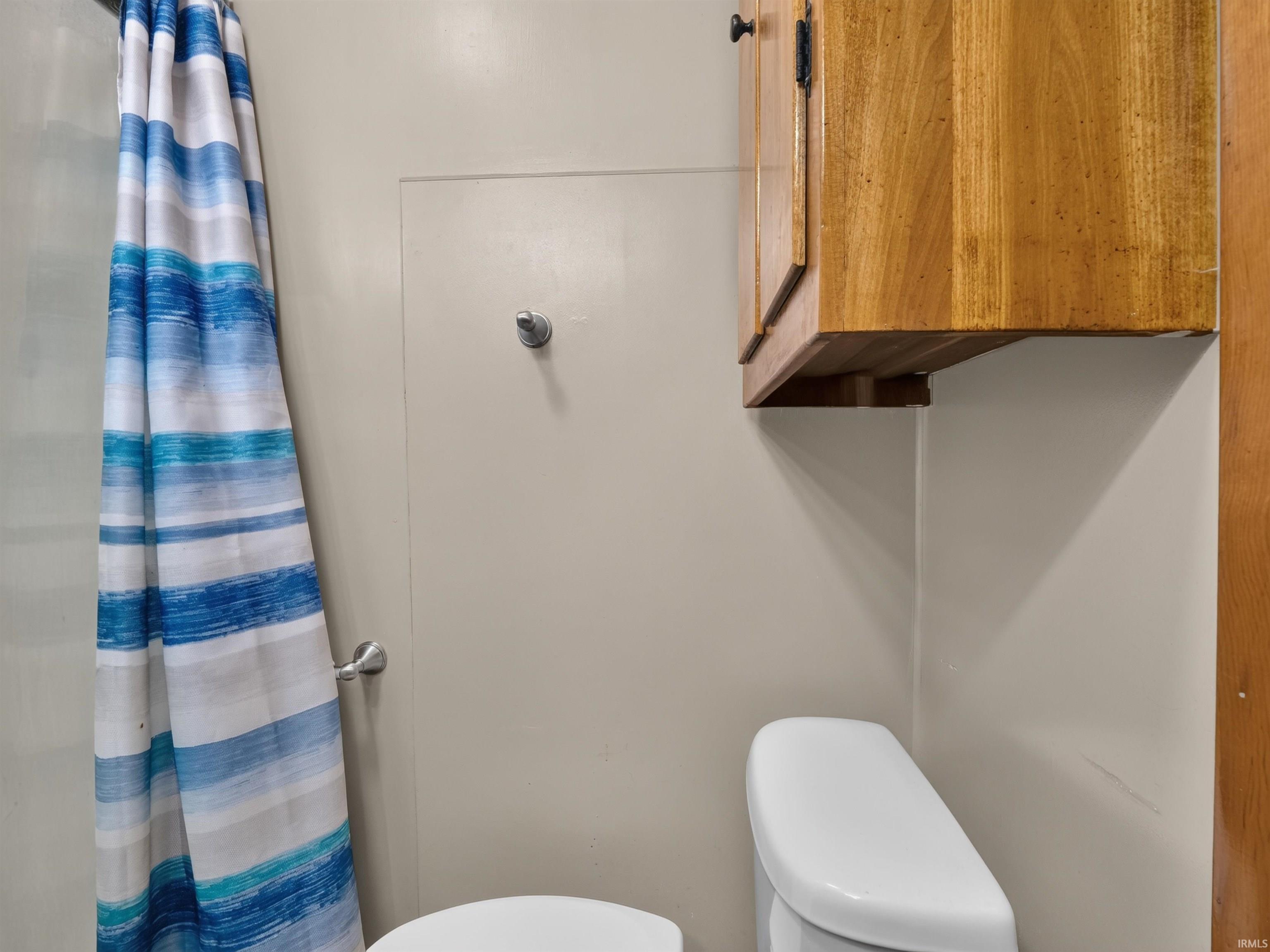 White commode with a wood-finish overhead cabinet and a wall-mounted hook