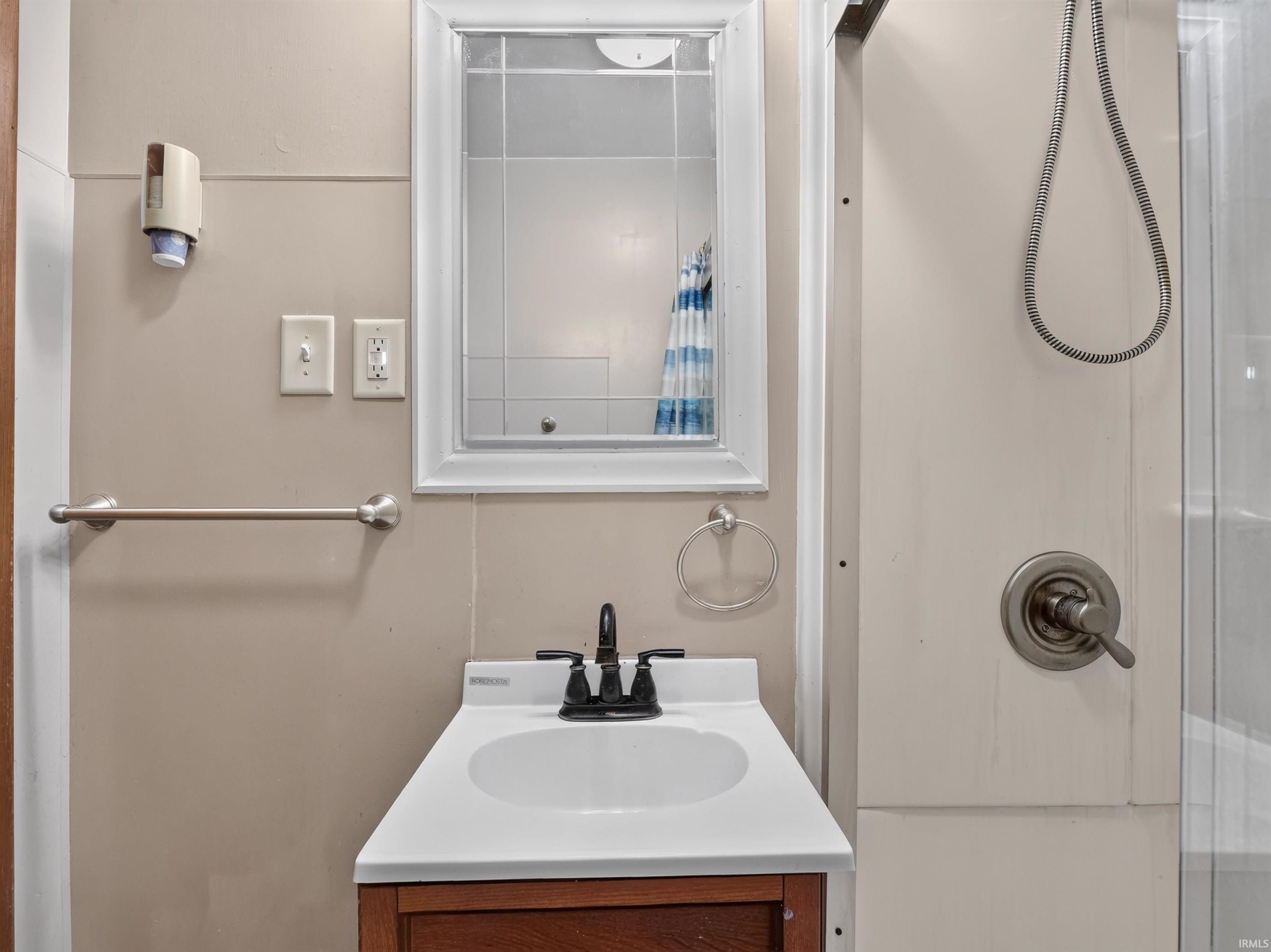 Bathroom vanity with a white countertop and dark wood-finish cabinetry, complemented by a wall-mounted mirror