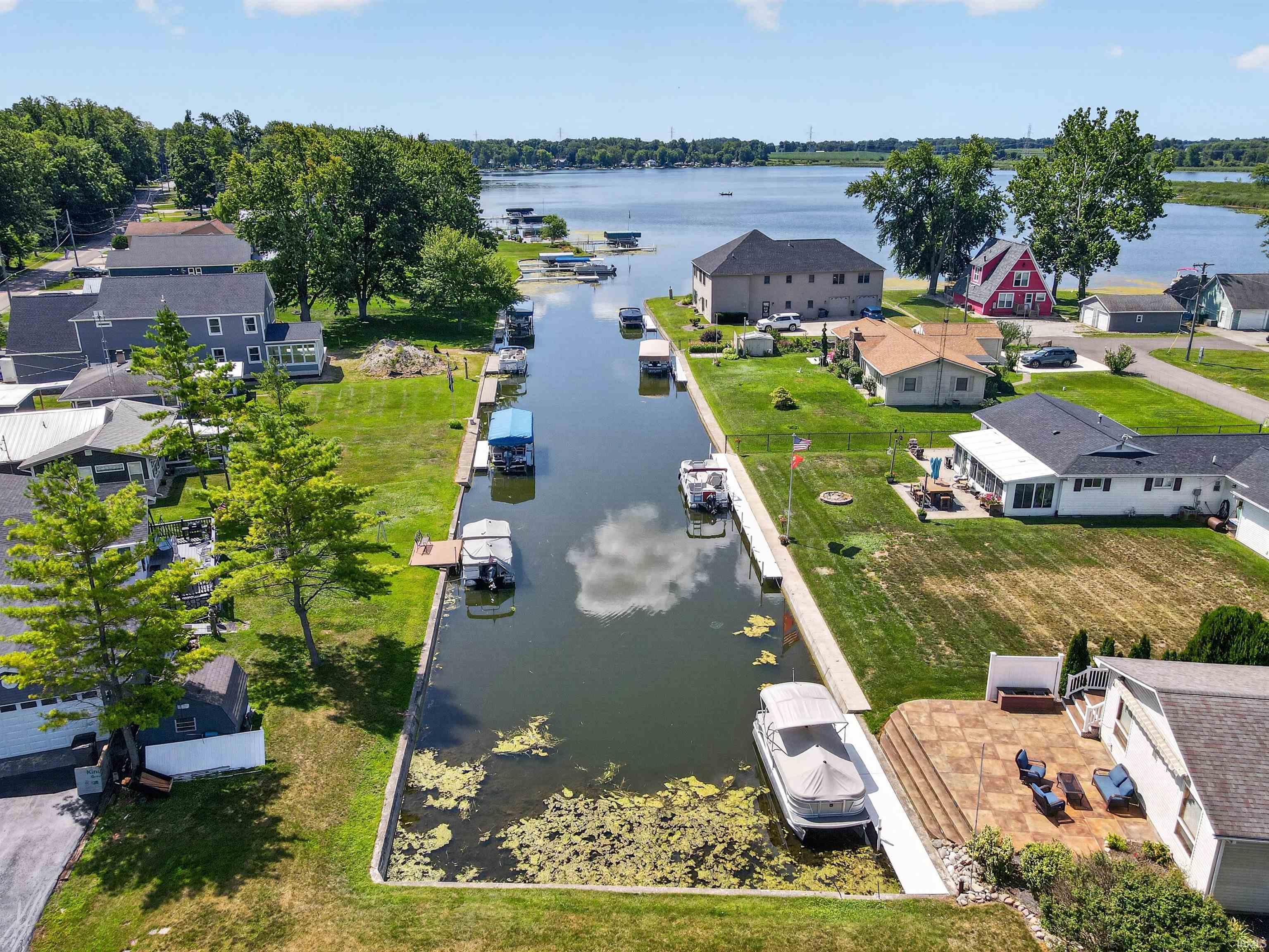 Waterfront property featuring extensive canal frontage, private boat docks, a large patio area with outdoor seating, and mature trees