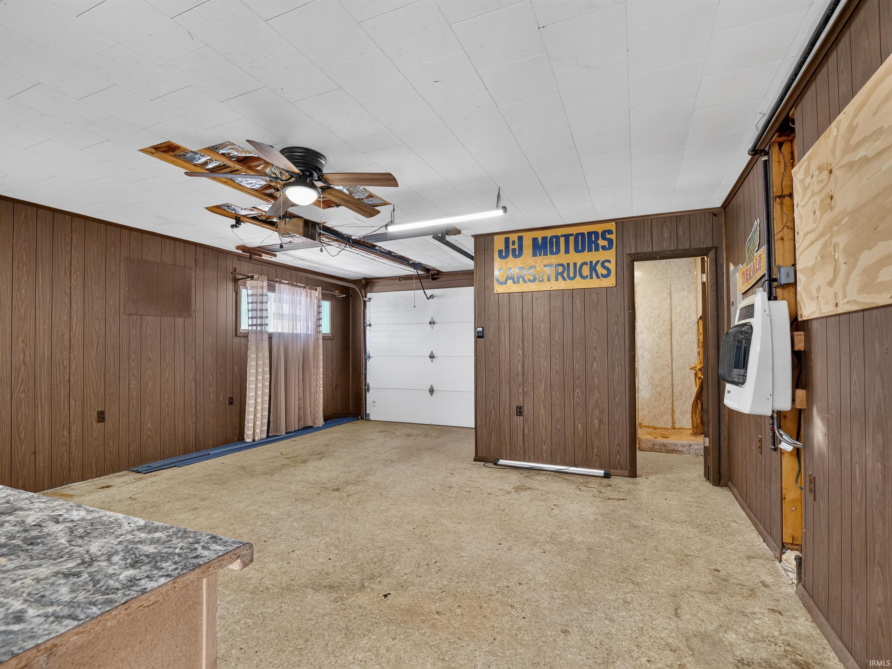 Garage space featuring wood-look paneling, a white paneled ceiling, and a ceiling fan with integrated lighting