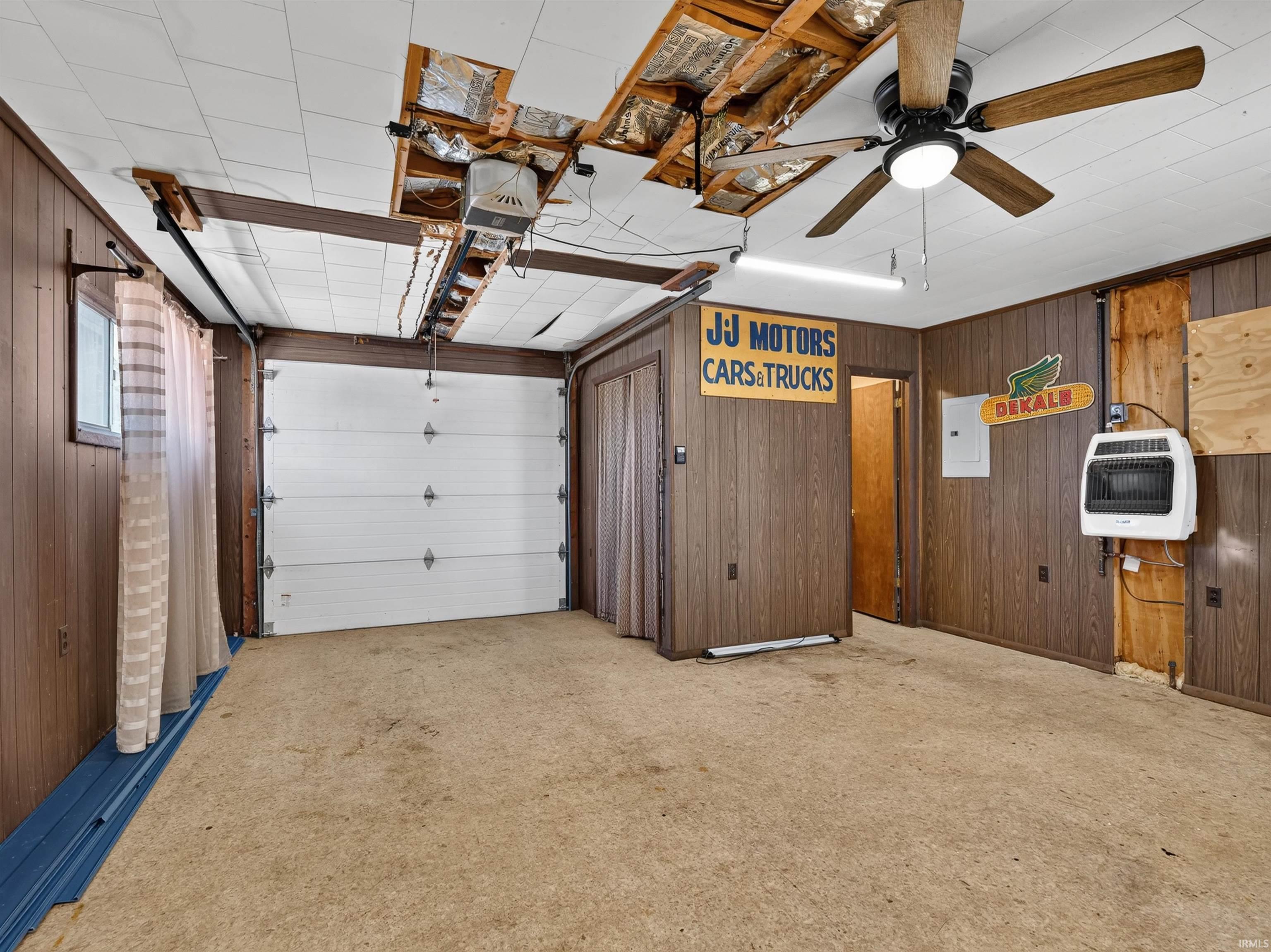 Carpeted interior space featuring wood paneling, a white overhead garage door, and a ceiling fan with integrated lighting