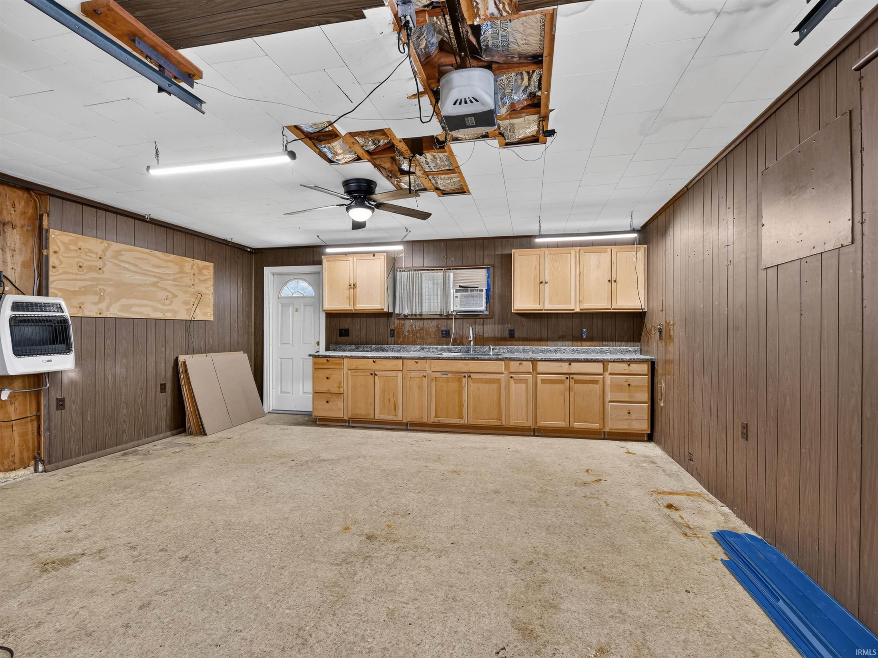 Utility space featuring wood paneling, a full run of wood cabinetry with a sink, and a white entry door with an arched window insert