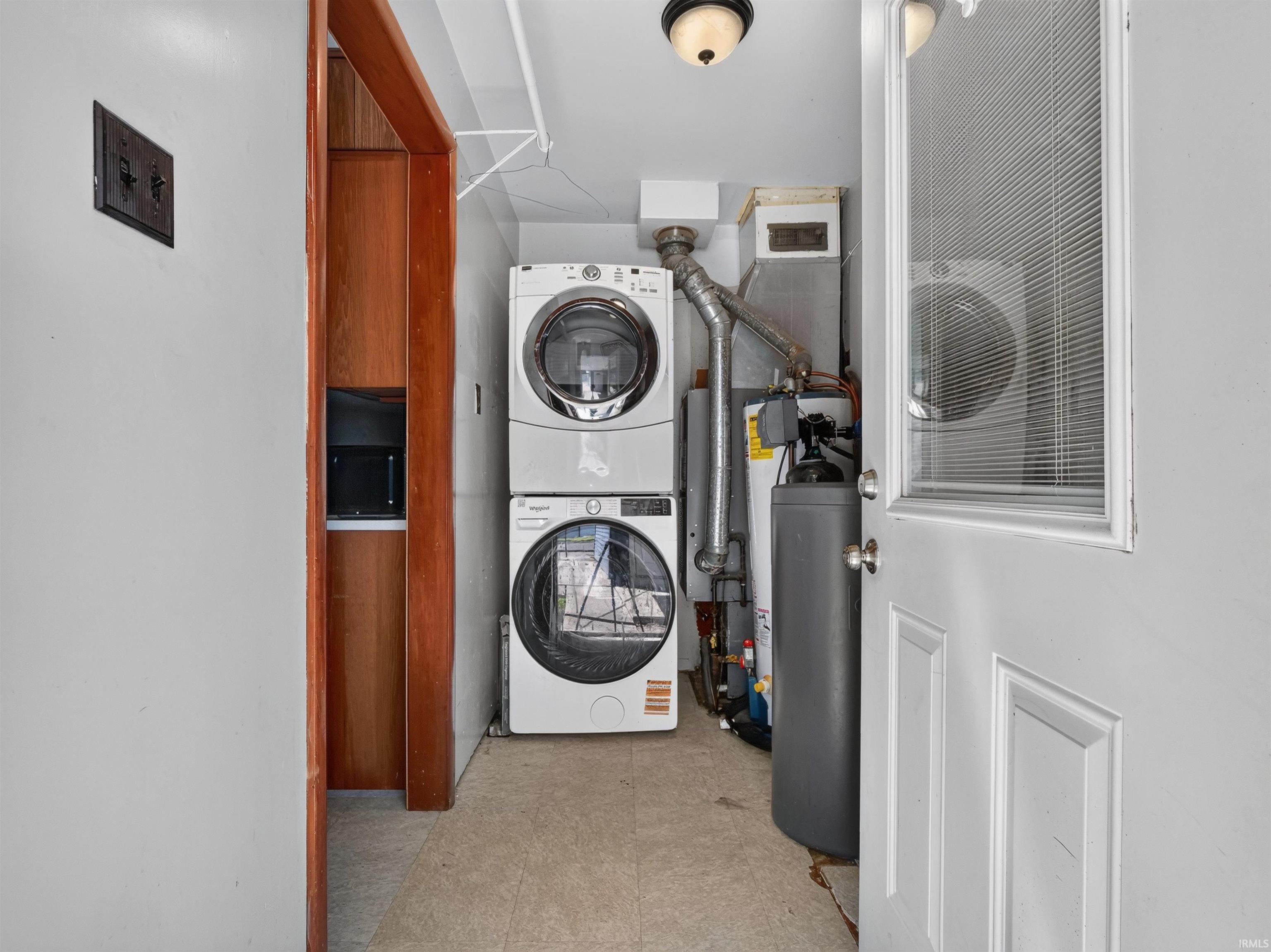 Dedicated laundry area featuring a stacked washer and dryer, water heater, and an adjacent built-in wooden cabinet