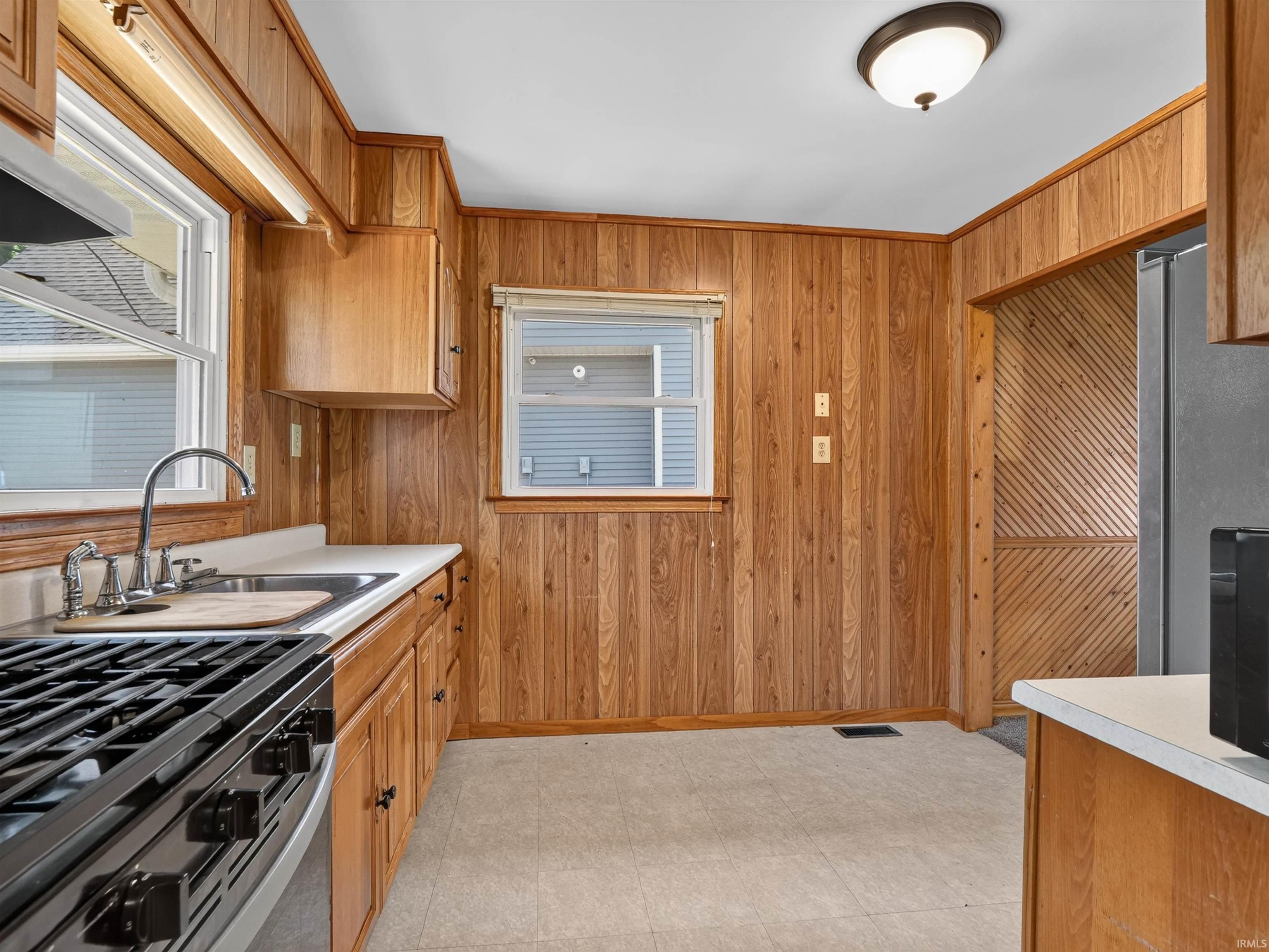 Kitchen with wood paneling, wood cabinetry, stainless steel range, and a dual-basin sink with a gooseneck faucet