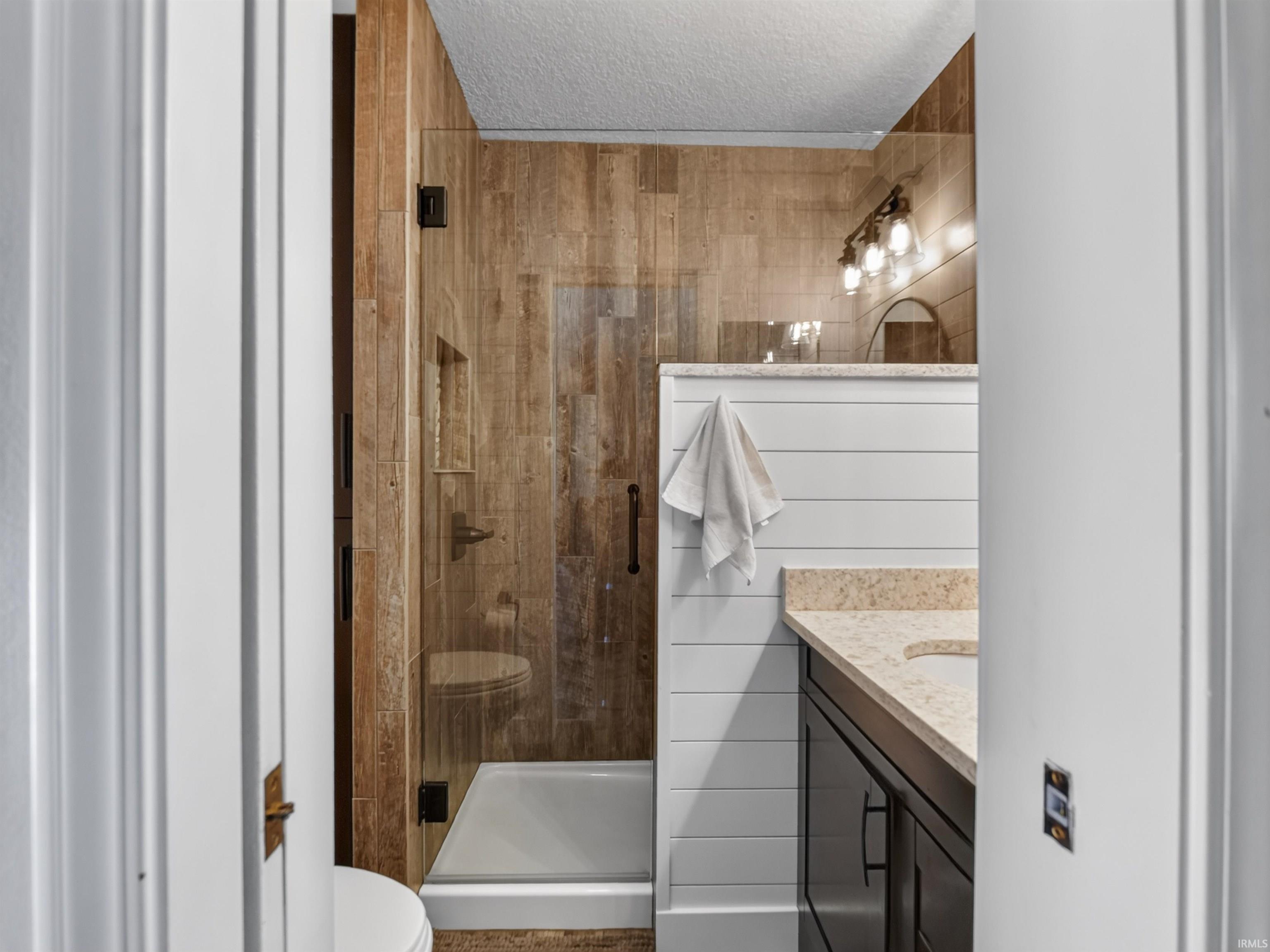 Bathroom featuring a glass-enclosed shower with wood-finish tile surround, a dark wood-finish vanity with a light-toned countertop, a rectangular sink, and shiplap paneling
