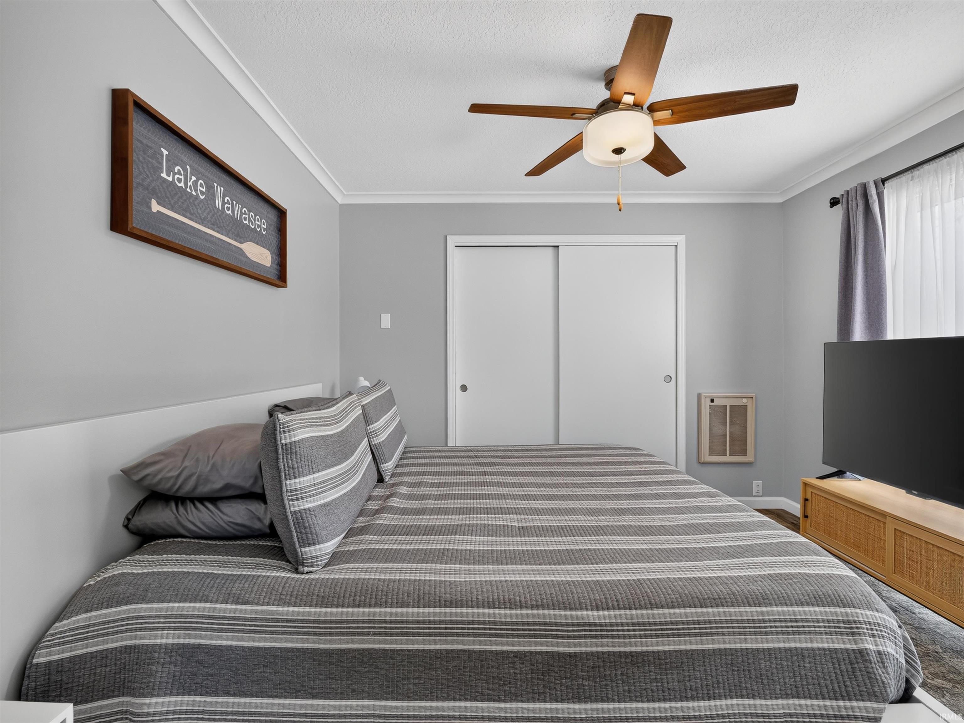 Bedroom featuring a ceiling fan with integrated lighting, crown molding, and sliding closet doors
