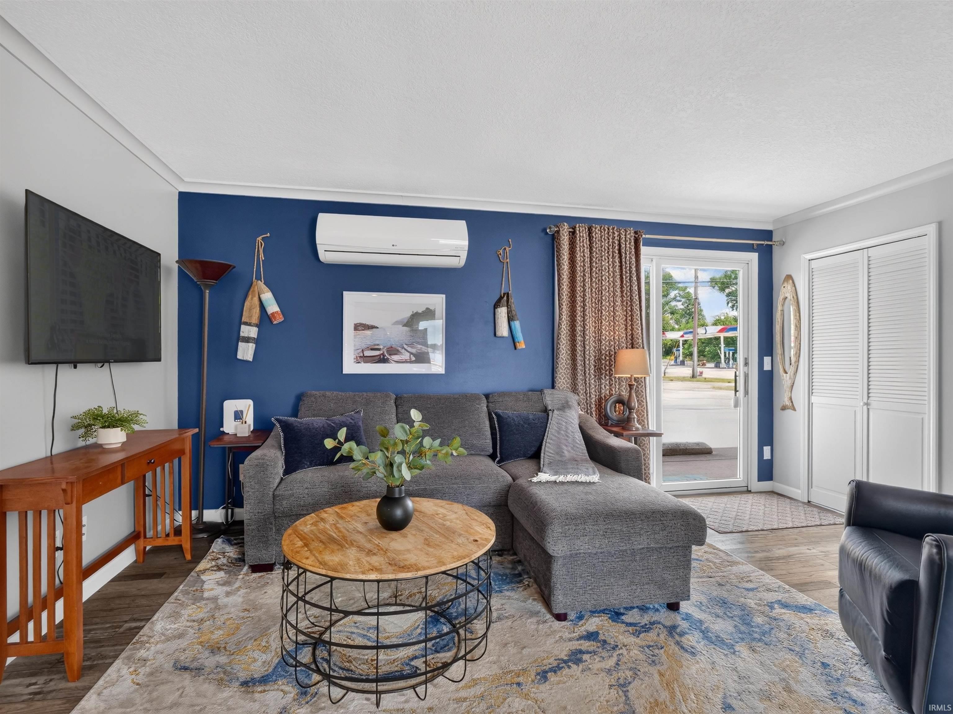 Living area featuring wood-finish flooring, crown molding, and a vibrant accent wall