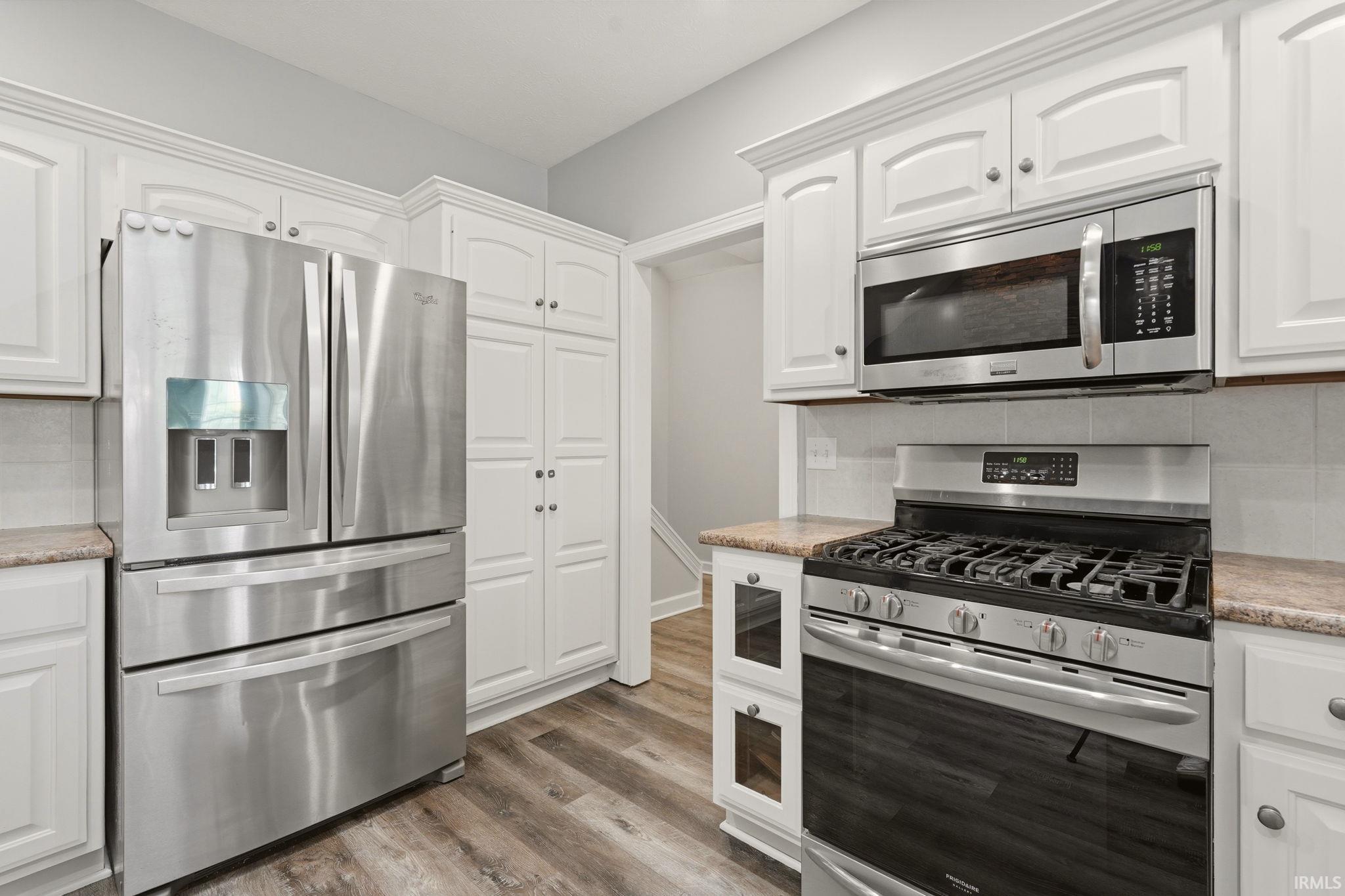 Kitchen featuring white cabinetry, stainless steel appliances, wood-finish flooring, and light-toned countertops