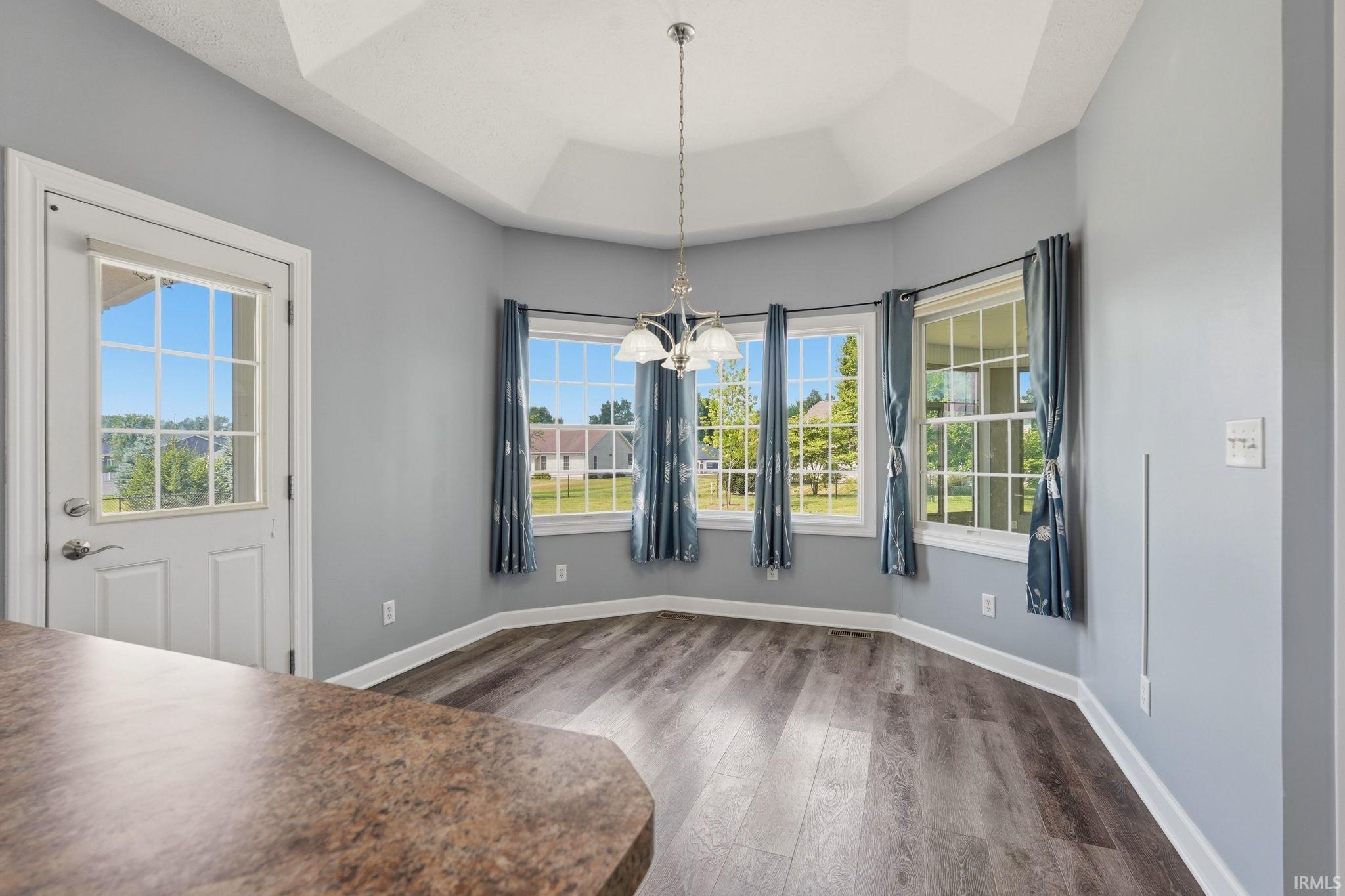 Informal dining space featuring a tray ceiling with a chandelier, wood-finish flooring, and multiple windows
