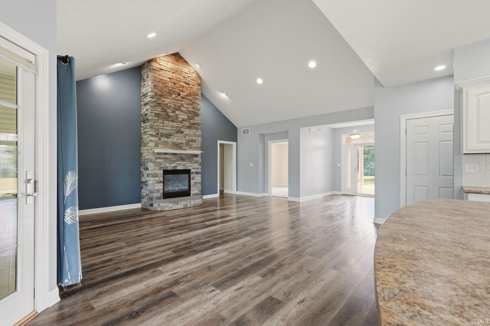 Spacious living area featuring a stone-clad fireplace with a built-in mantel, high vaulted ceilings, recessed lighting, and wood-finish flooring