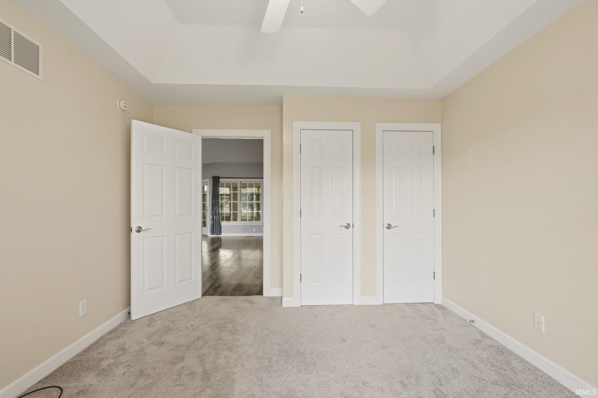Bedroom featuring light neutral paint, tray ceiling, and soft gray carpet