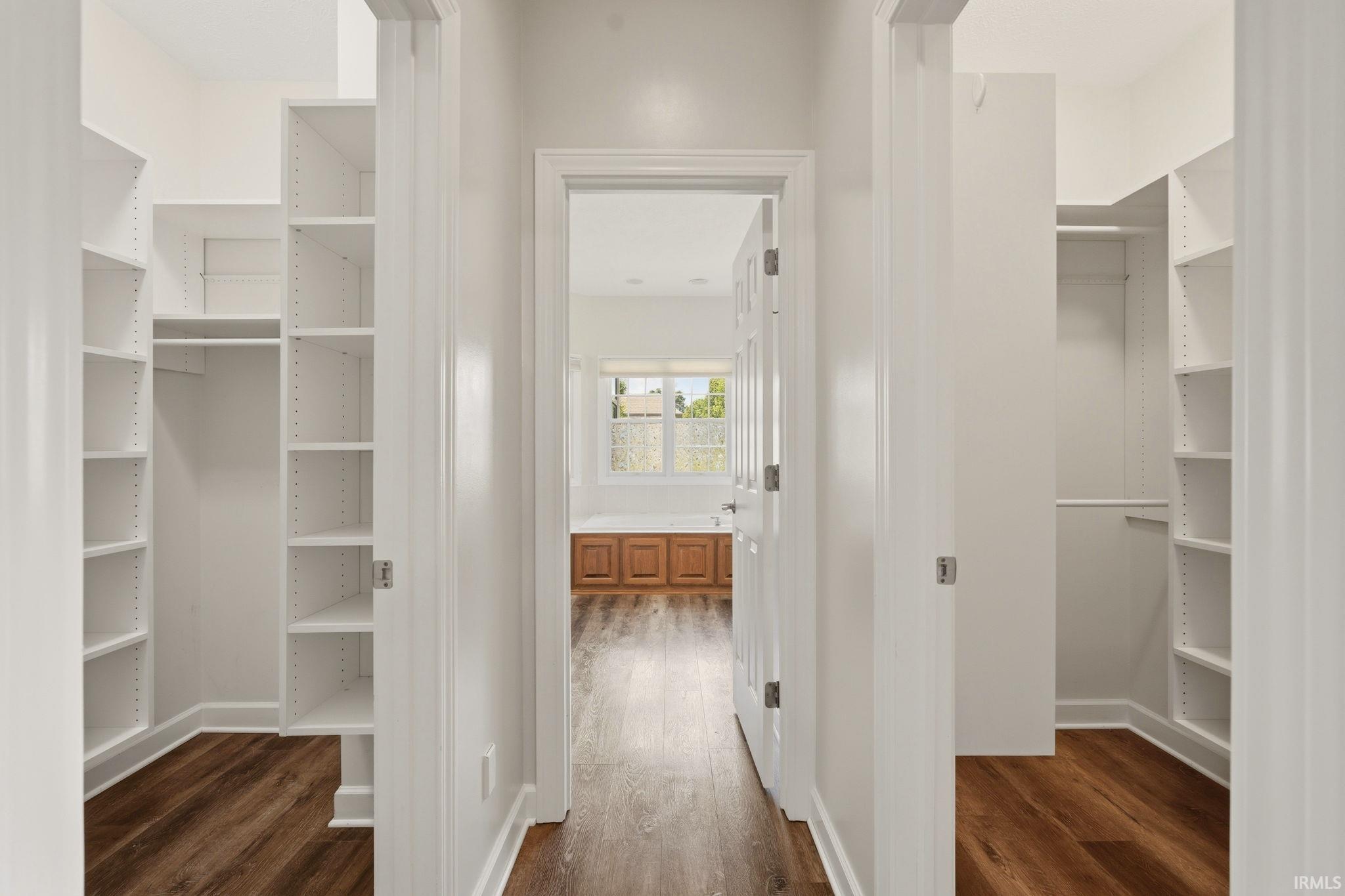 Hallway featuring dual walk-in closets with extensive built-in shelving and hanging rods