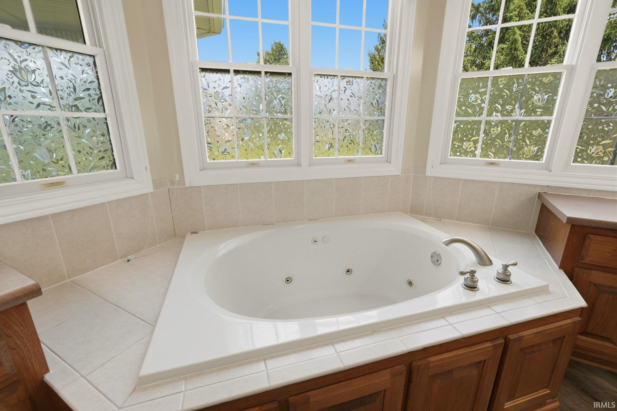 Built-in jetted tub surrounded by neutral-toned tile and wood-finish cabinetry
