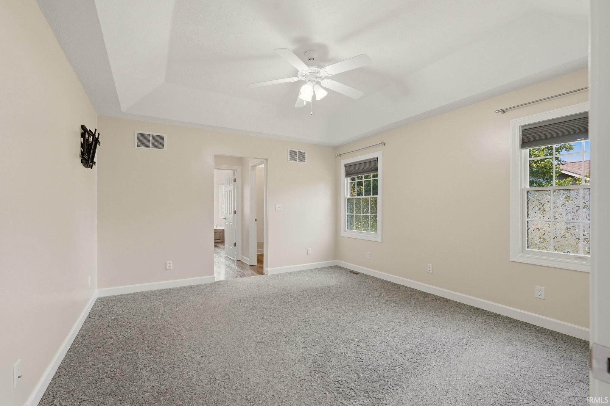 Spacious room featuring vaulted ceilings, a ceiling fan, two windows with roller shades, and patterned gray carpeting