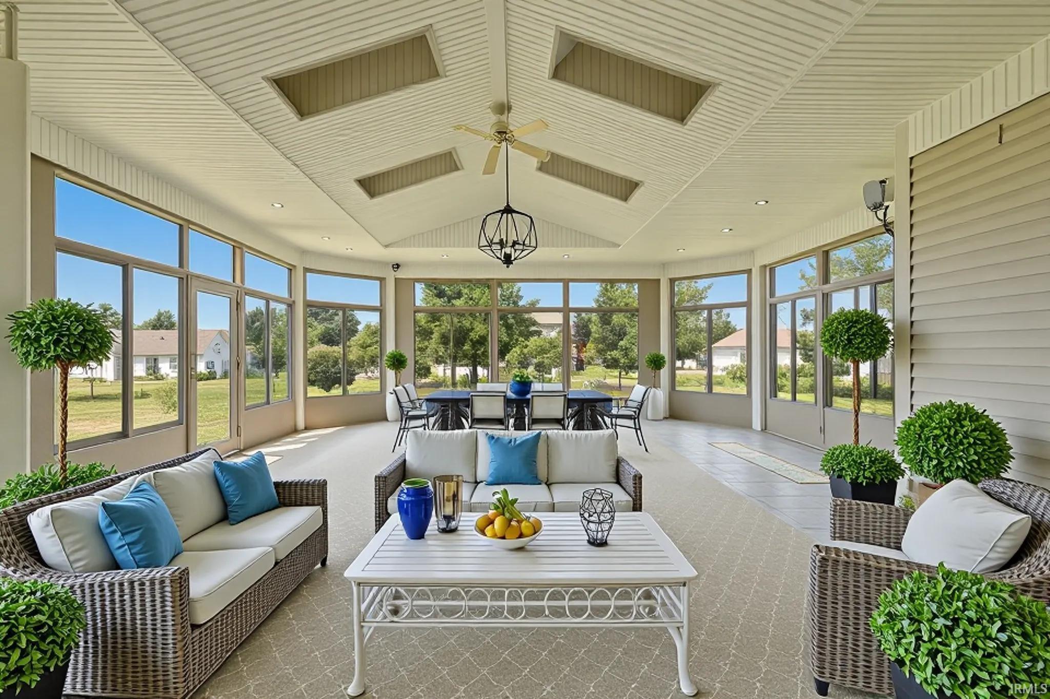 Spacious sunroom featuring a vaulted ceiling with skylights, extensive window walls, and a ceiling fan