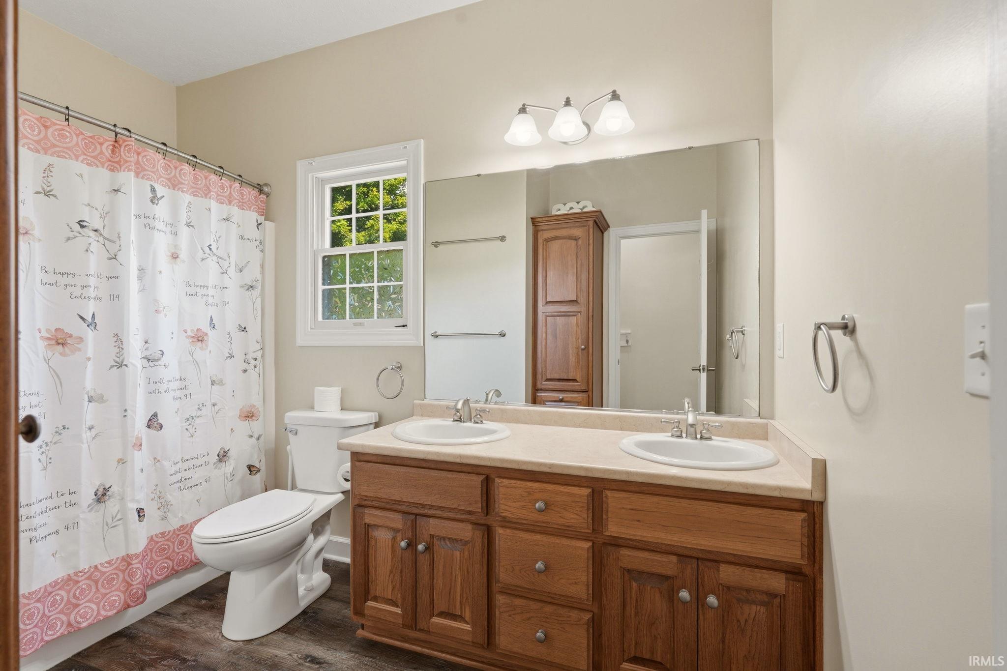 Bathroom with a double vanity featuring wood-finish cabinetry and integrated sinks, a window with exterior views, and wood-finish flooring