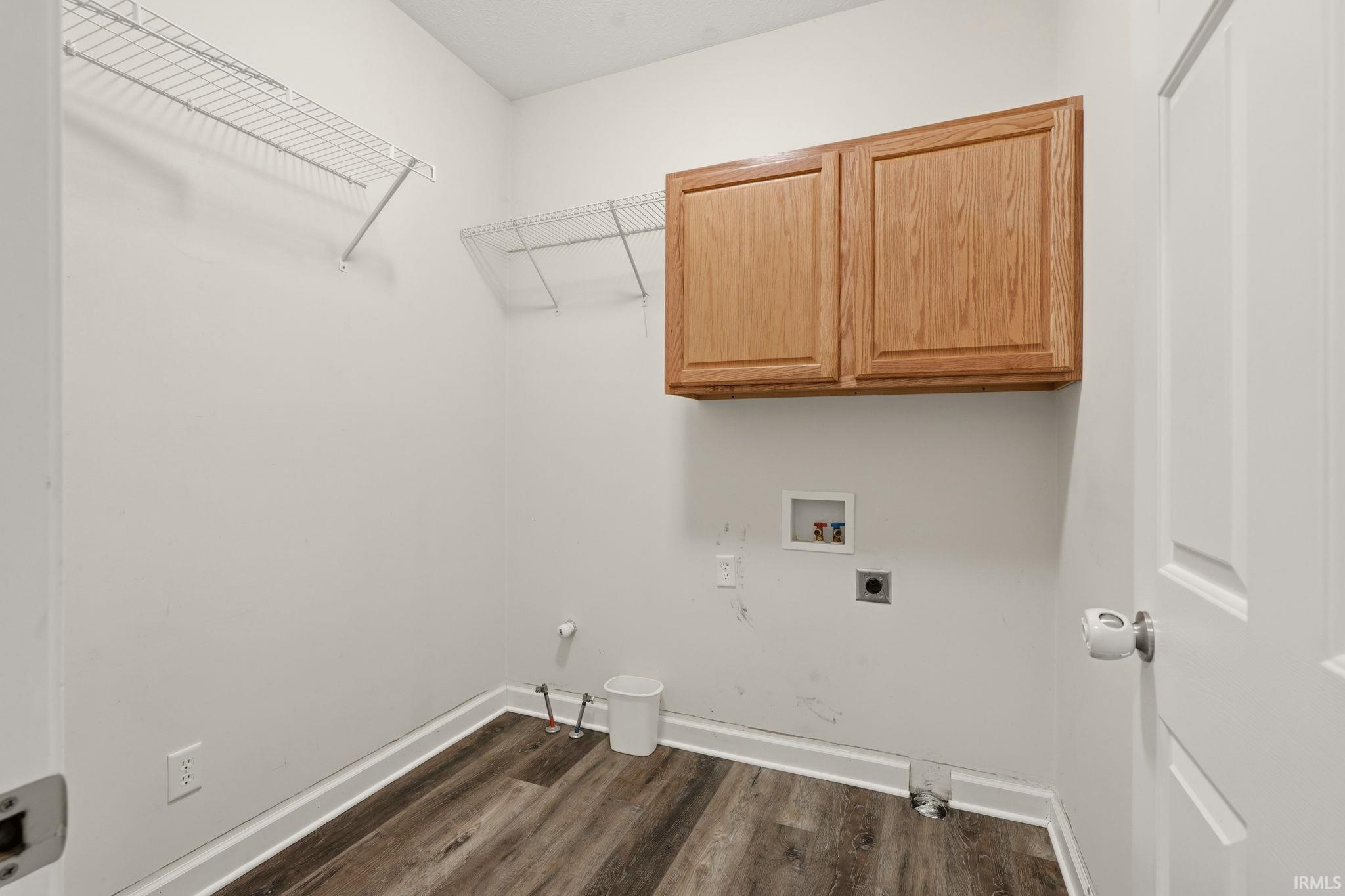 Dedicated utility space featuring wood-finish flooring, white wire shelving, wall-mounted wood cabinetry, and essential plumbing hookups