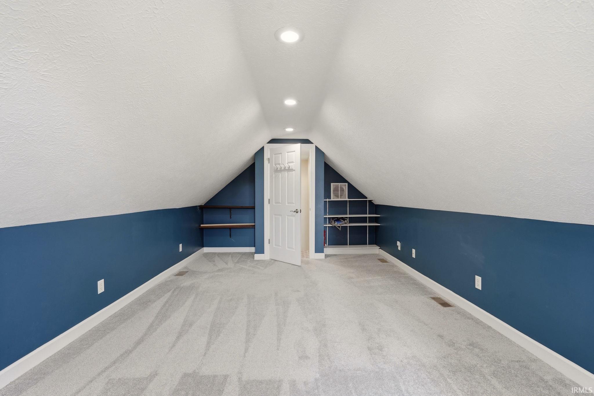 Spacious attic room featuring sloped ceilings, recessed lighting, and light gray patterned carpeting