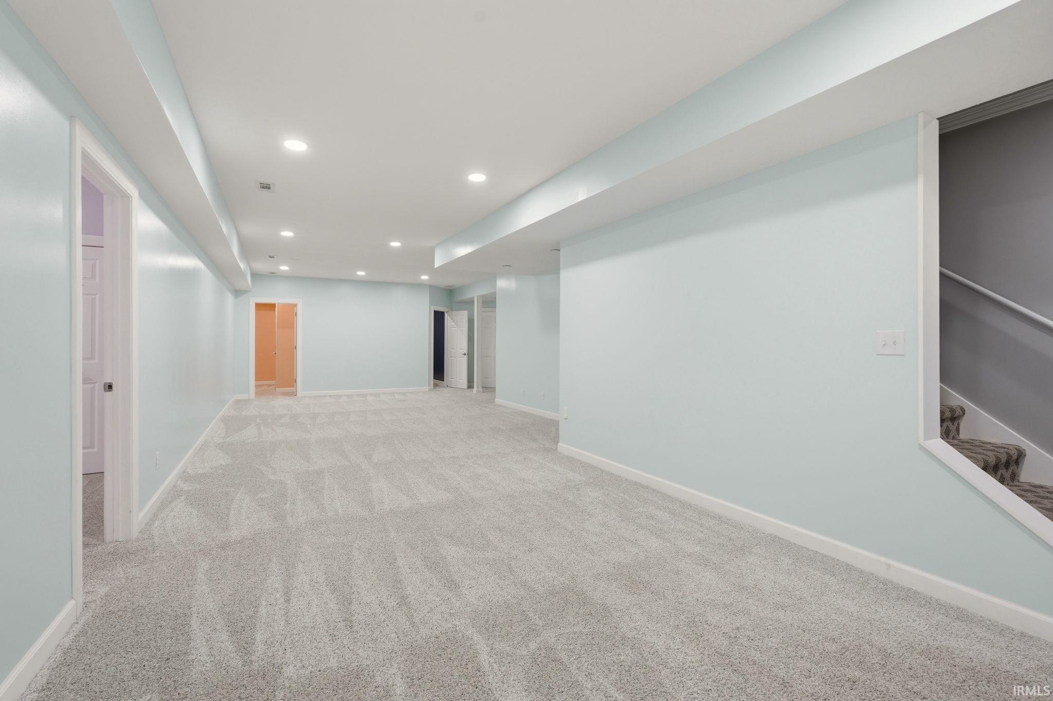 Spacious lower level featuring plush patterned carpeting, light blue wall paint, recessed lighting, and white trim