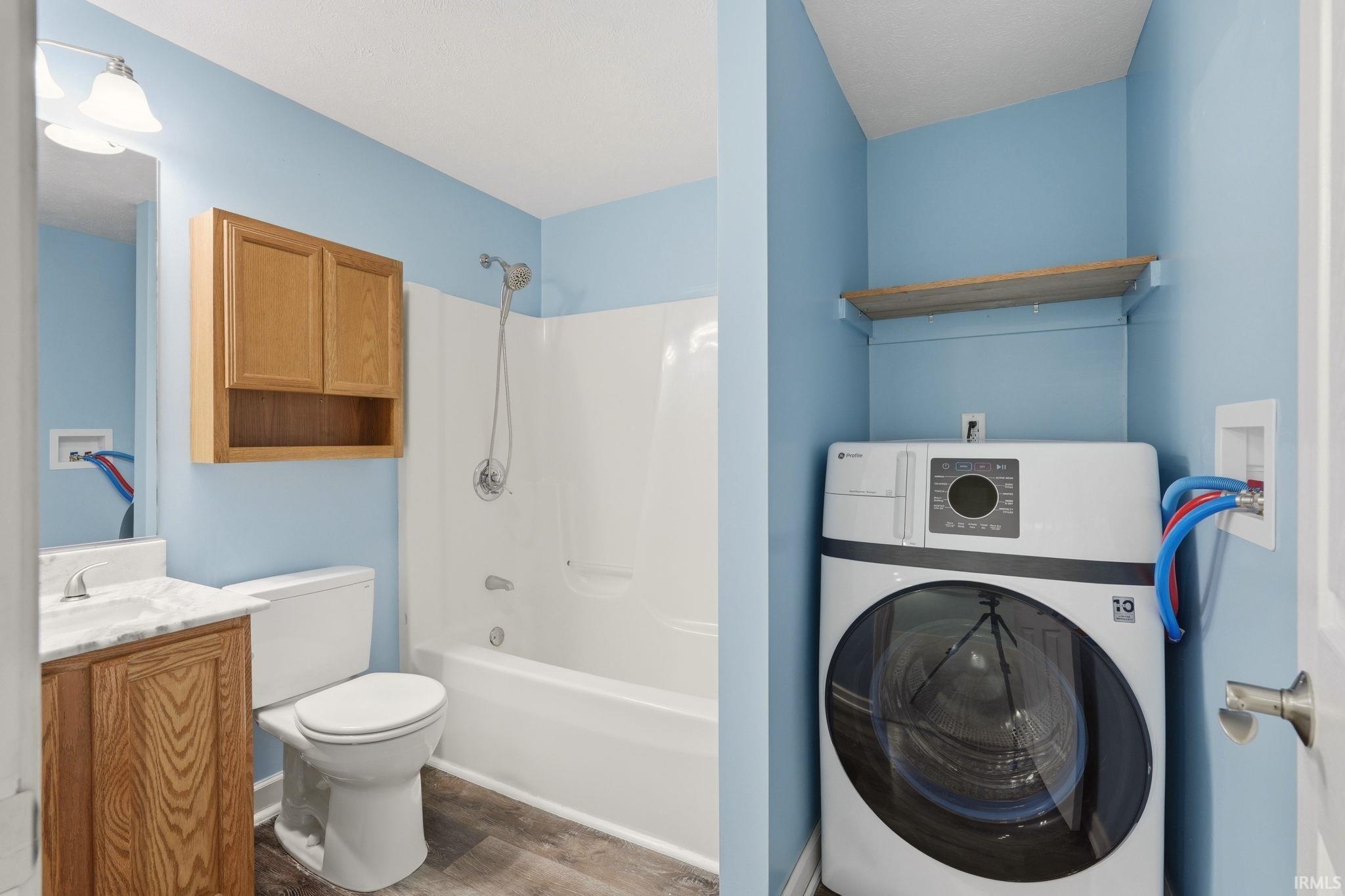 Full bathroom featuring a white tub/shower combination with chrome fixtures, a wood-finish vanity with a white countertop and integrated sink, a toilet, and a built-in wall cabinet