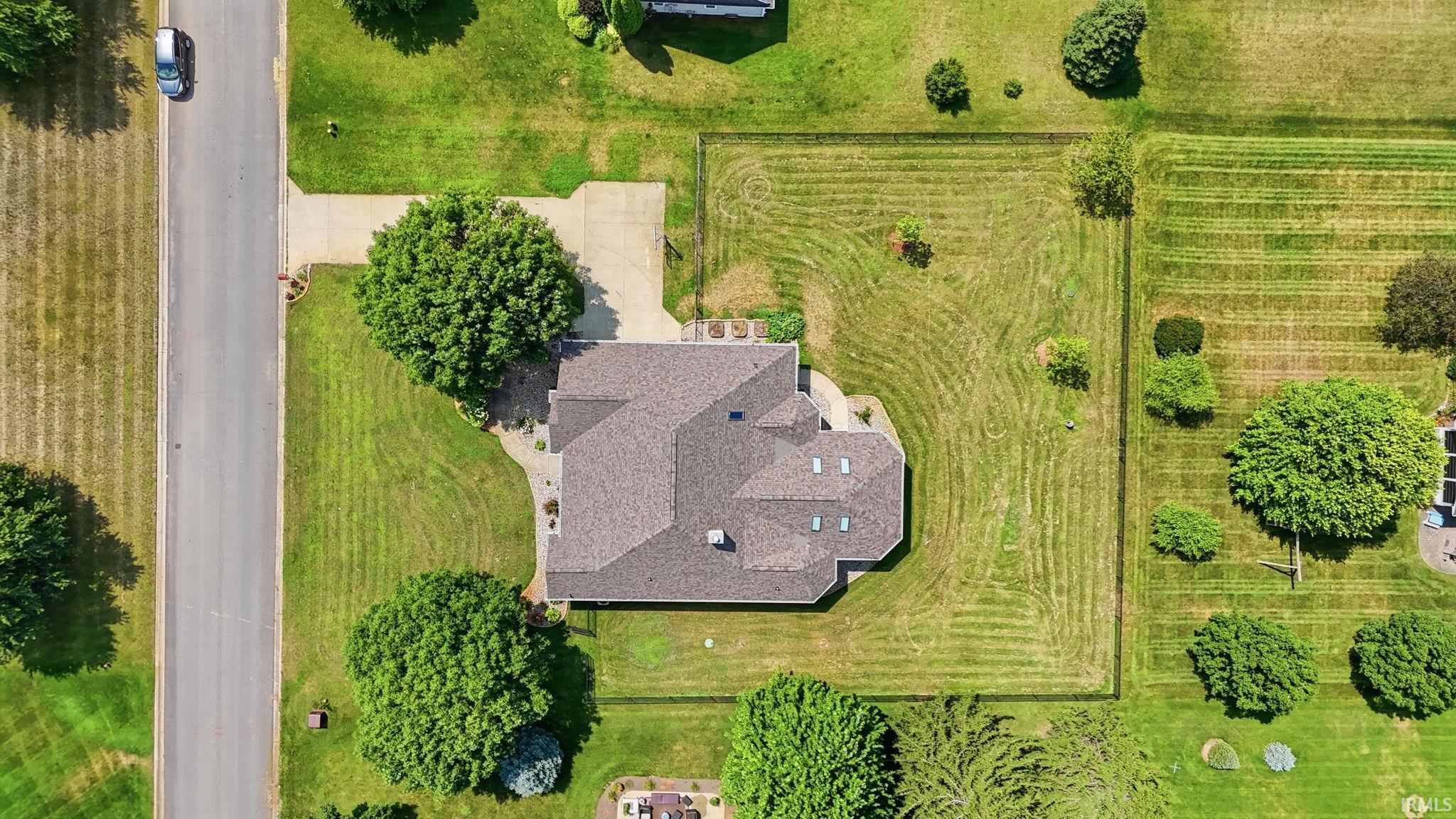 Property featuring a dark shingled roof, a paved driveway, and extensive green lawns