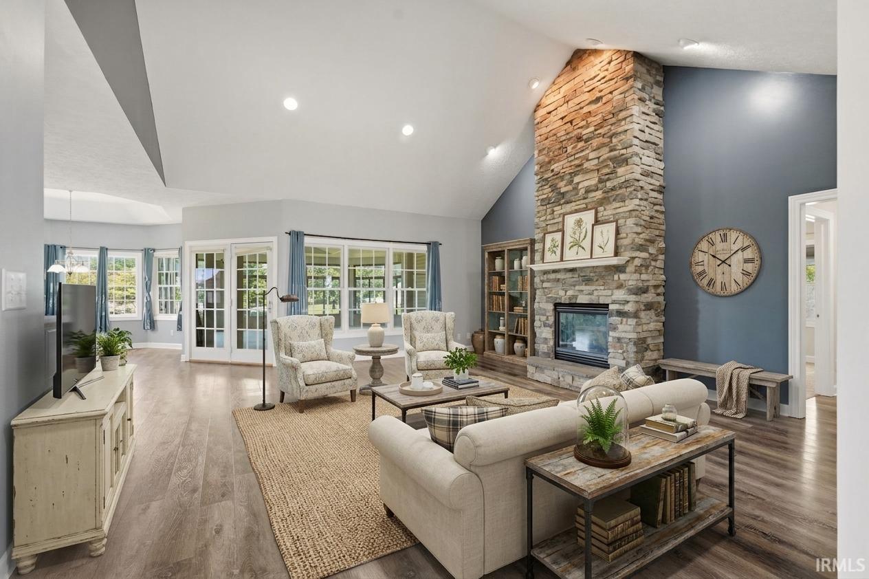 Vaulted ceilings, a floor-to-ceiling stone fireplace, wood-finish flooring, recessed lighting, and expansive windows