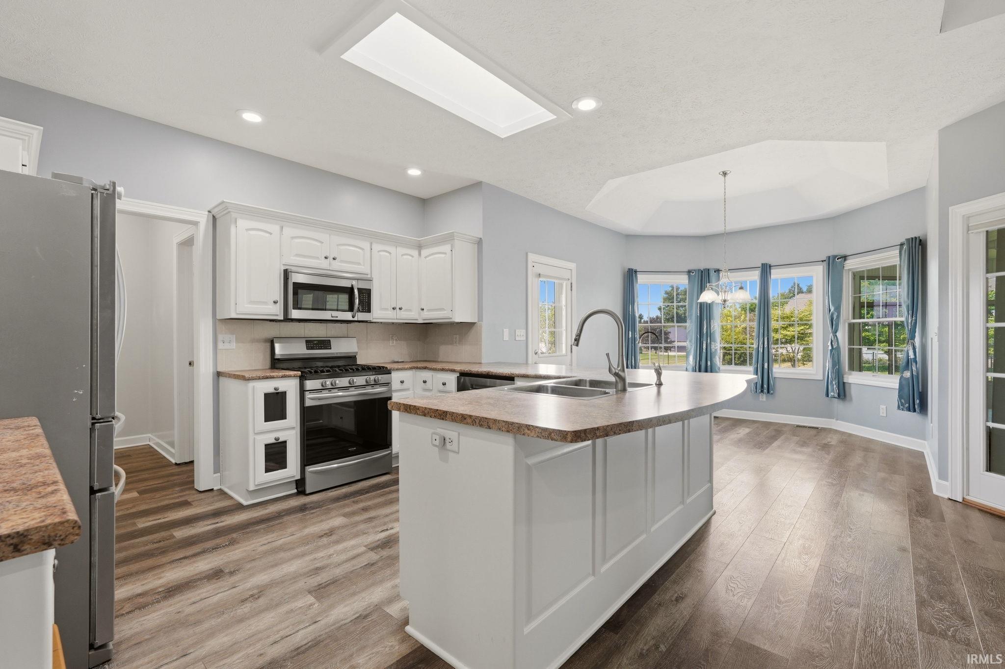 Open-concept kitchen featuring white cabinetry, stainless steel appliances, and wood-finish flooring