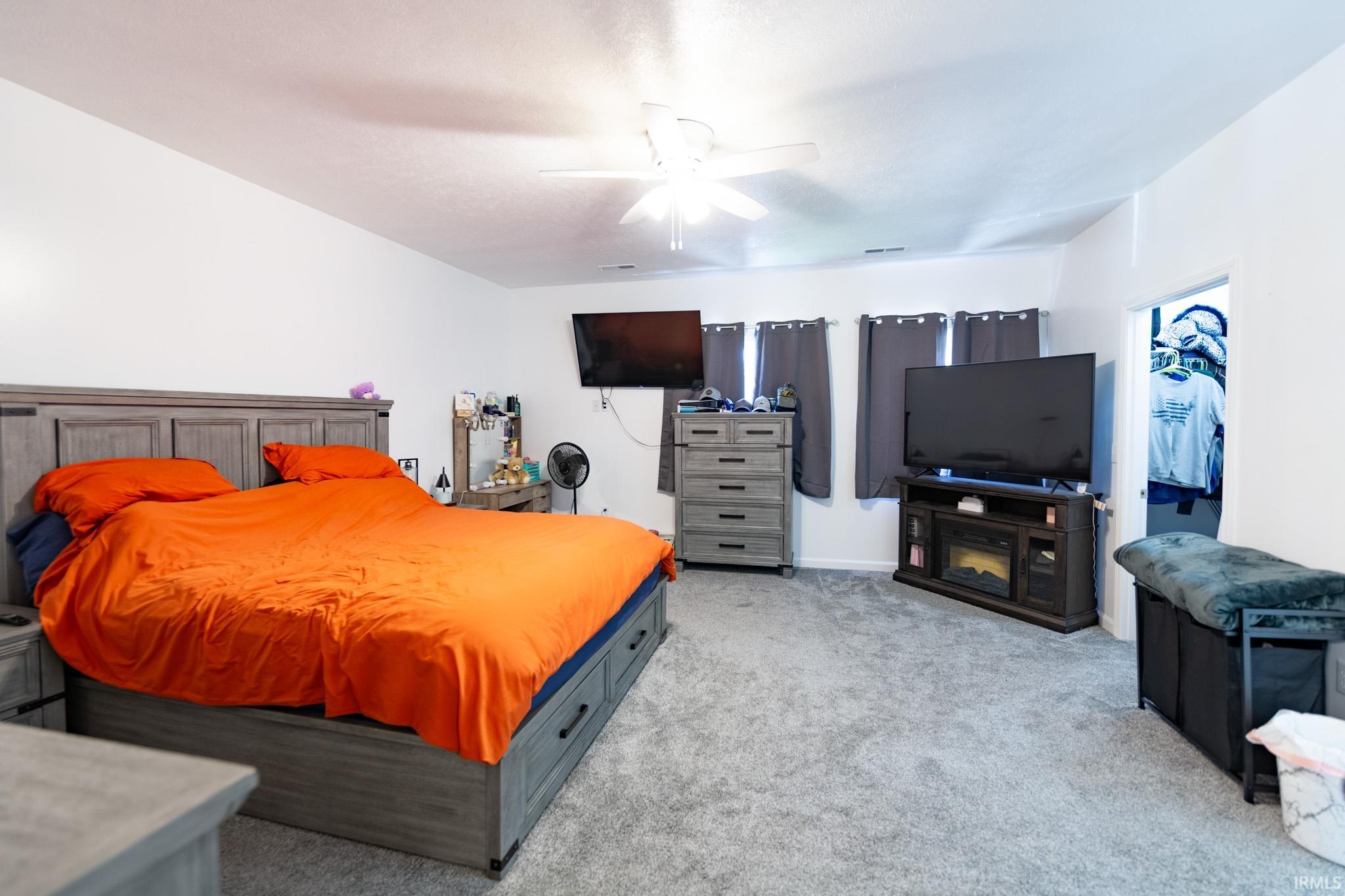 Spacious bedroom featuring light gray carpeting, neutral wall finishes, and a ceiling fan